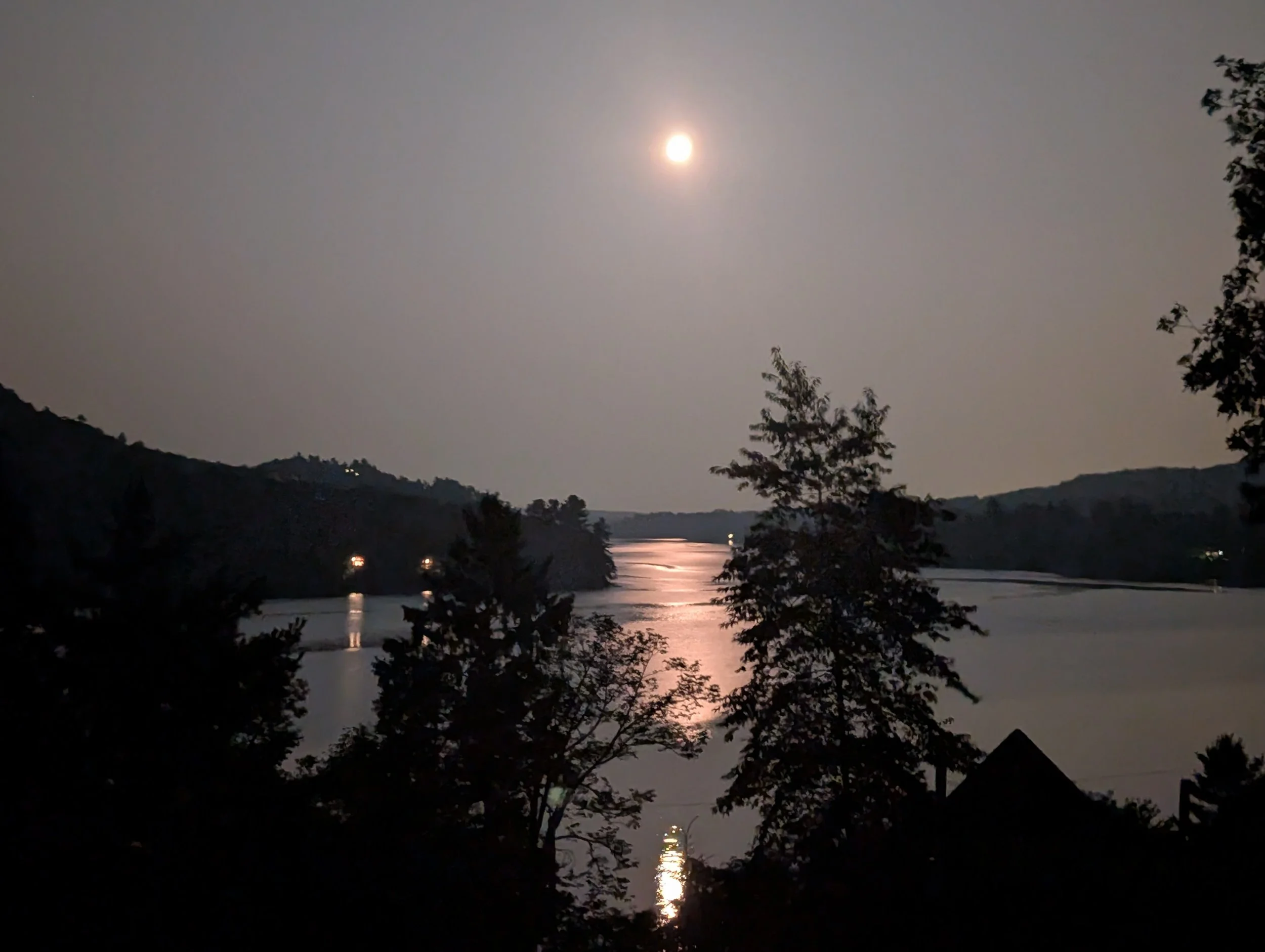 Nighttime scene of a river under the light of a full moon, with silhouettes of trees and hills.