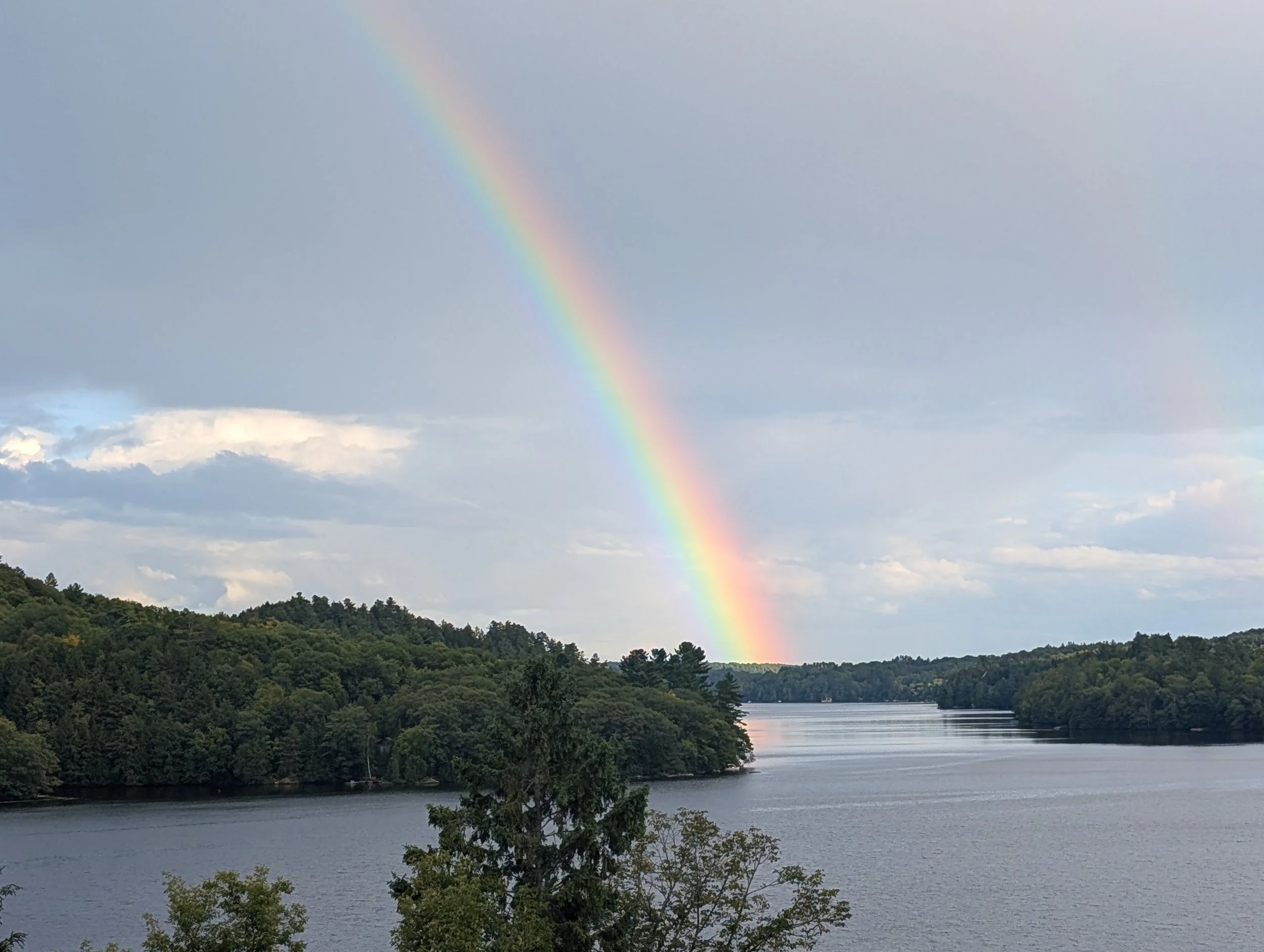 A rainbow over a large lake surrounded by green trees and hills.