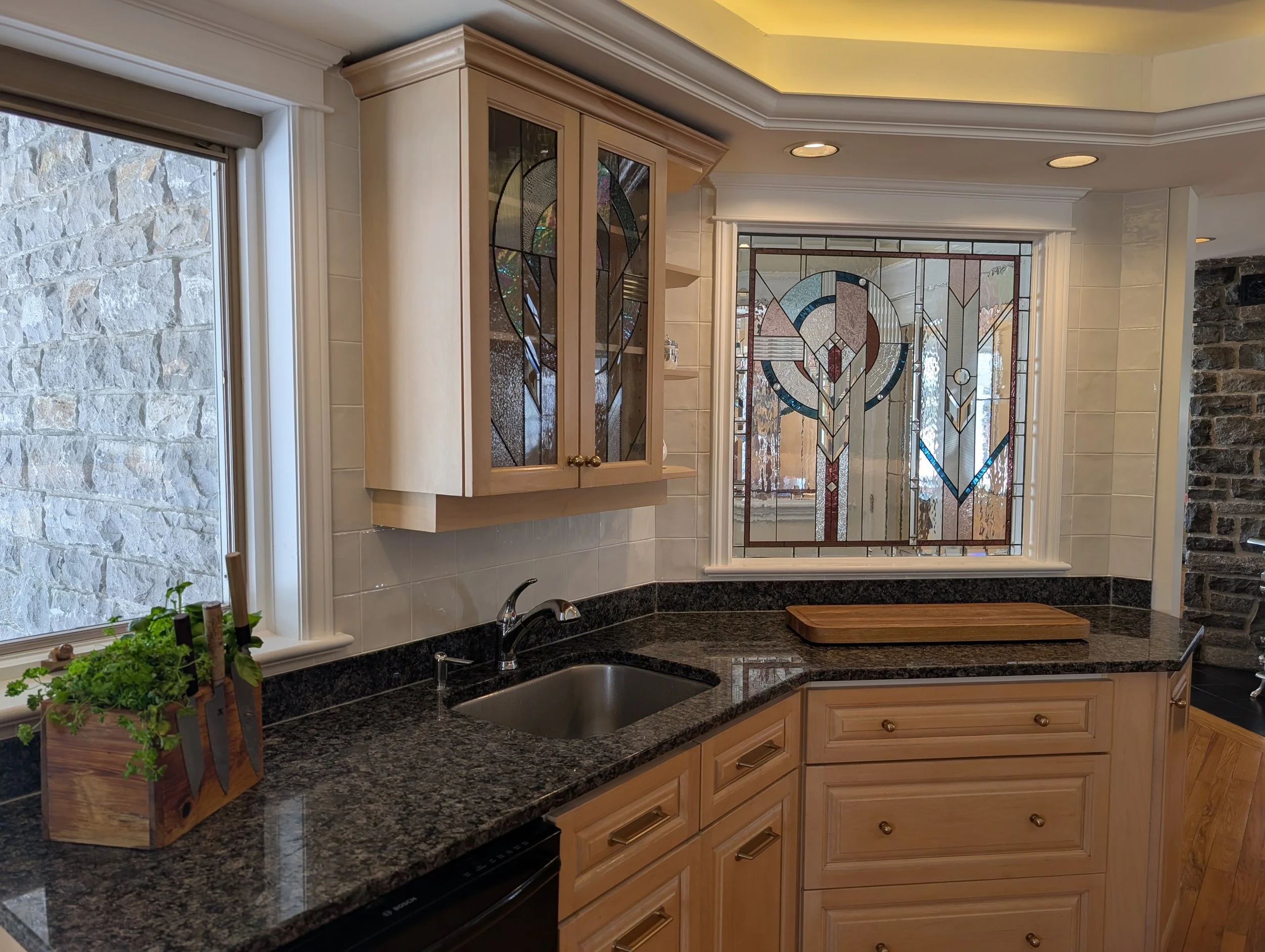 Kitchen with granite countertops, light wood cabinets, stained glass window, and a small potted herb plant on the counter.