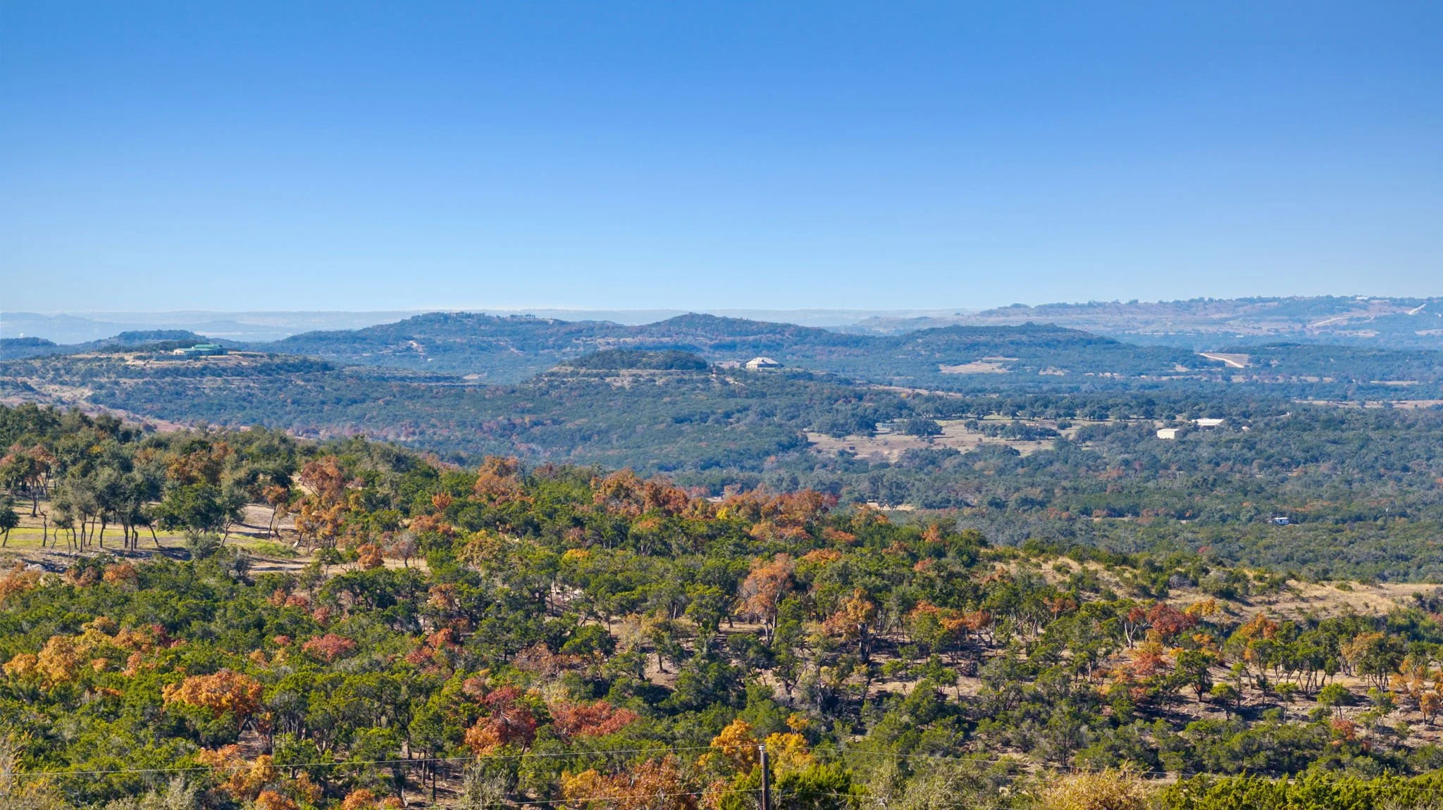 A scenic landscape of rolling hills covered in green and autumn-colored trees under a clear blue sky.