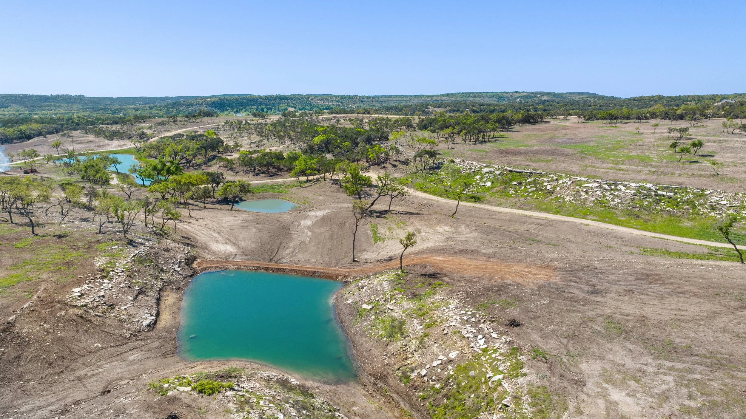 A landscape with multiple small bodies of water surrounded by sparse trees and dry land, showing signs of drought.