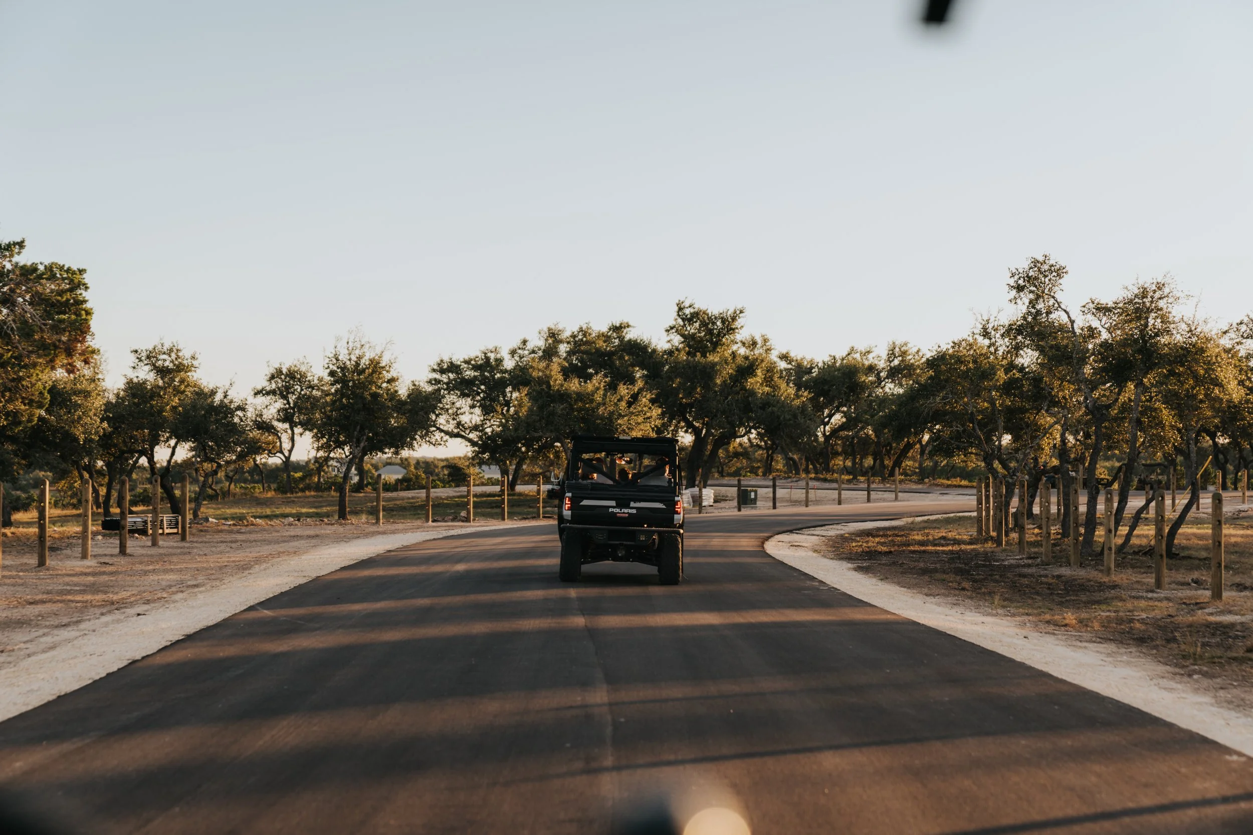 A black Polaris off-road vehicle driving on a paved road surrounded by trees with green foliage.
