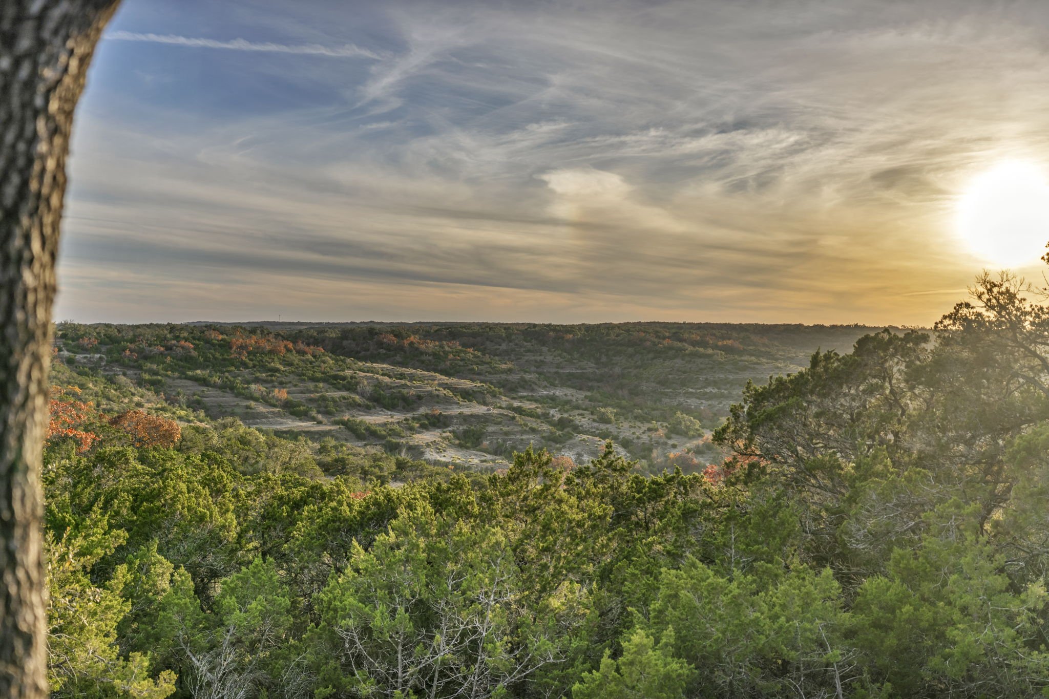 Scenic view of a sunset in the distance at RanchesAt Dripping Springs, looking over a lush green valley with trees and rolling hills in the distance, 