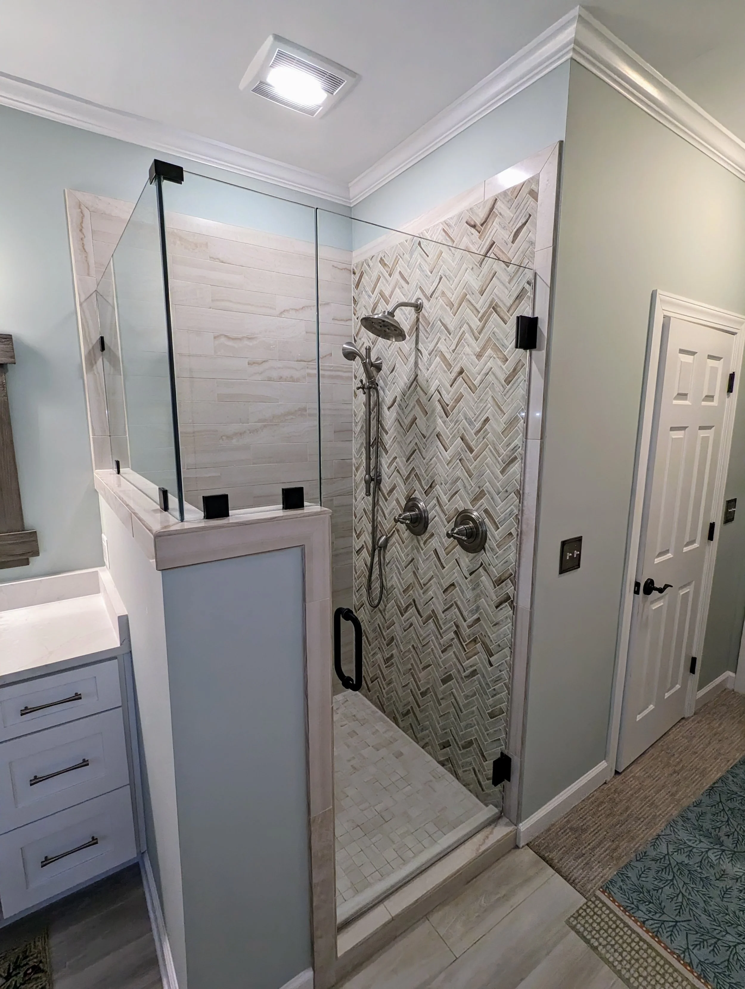 Bathroom shower with glass door, tile walls in herringbone pattern, and a handheld showerhead