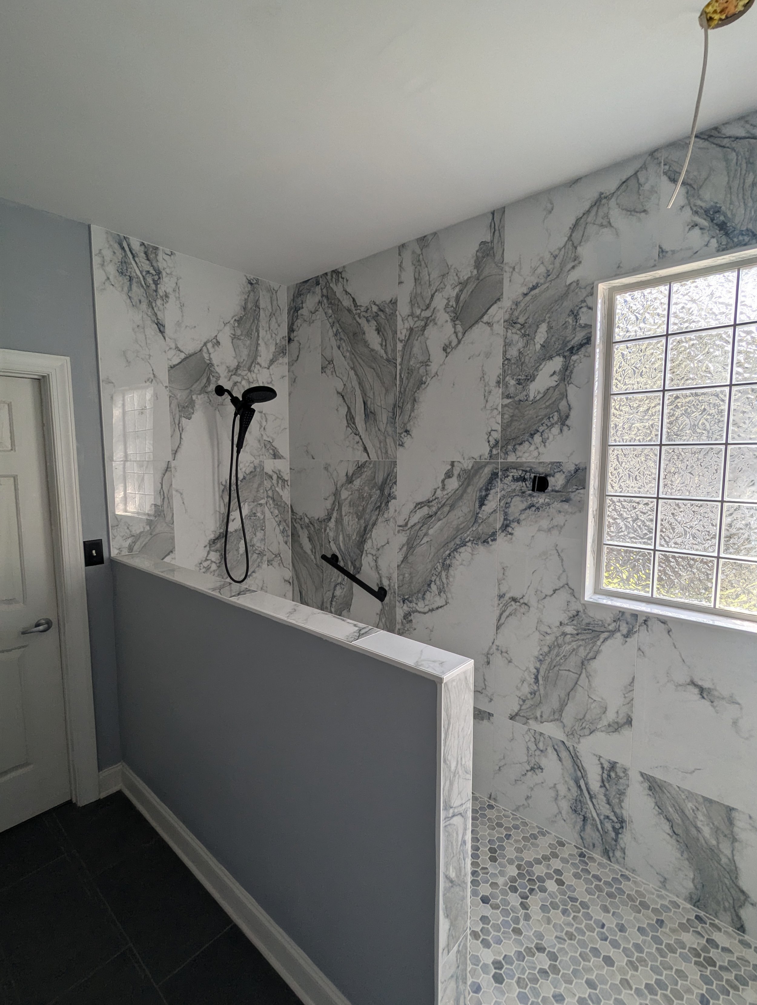 Bathroom with marble tile walls, a frosted glass block window, a showerhead, and a partial wall divider.