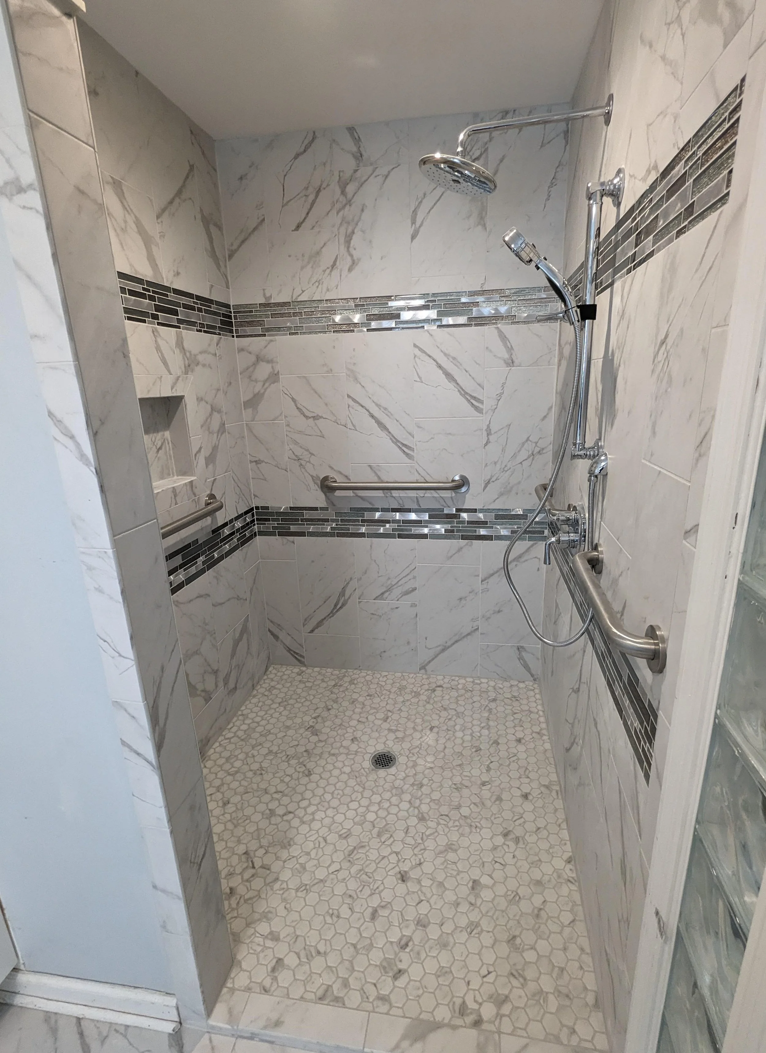 Accessible shower with marble tiles, two grab bars, and a hand-held shower head.