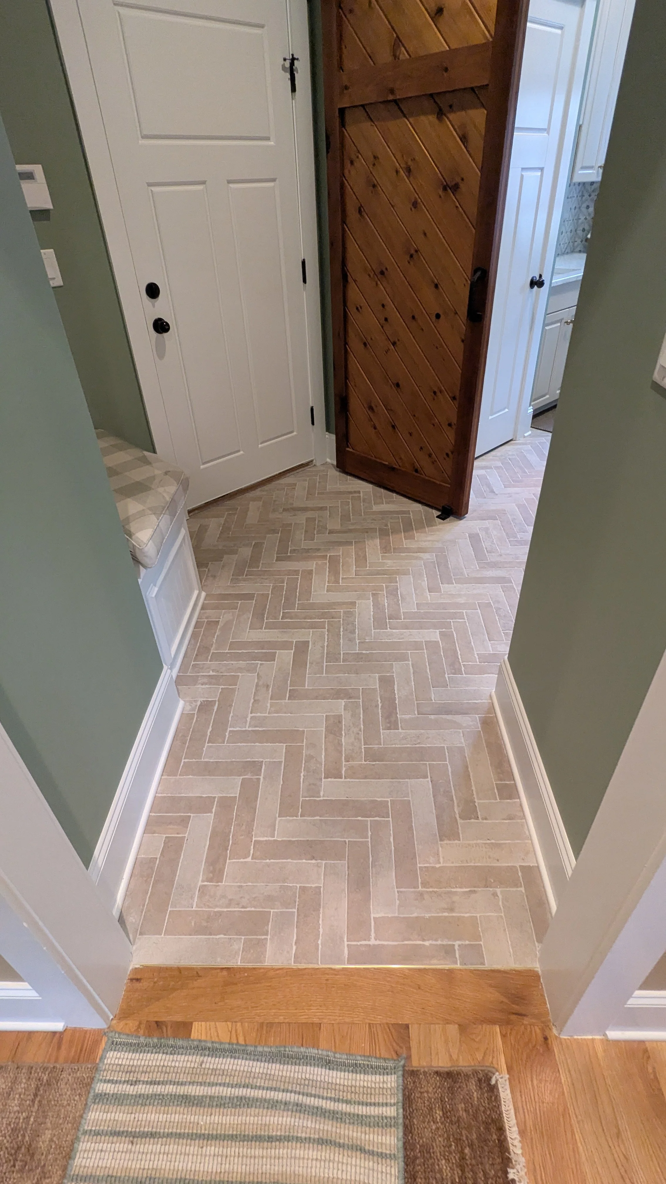 Interior view of a house entryway with a beige tile herringbone floor, green walls, white door, and wooden sliding door.