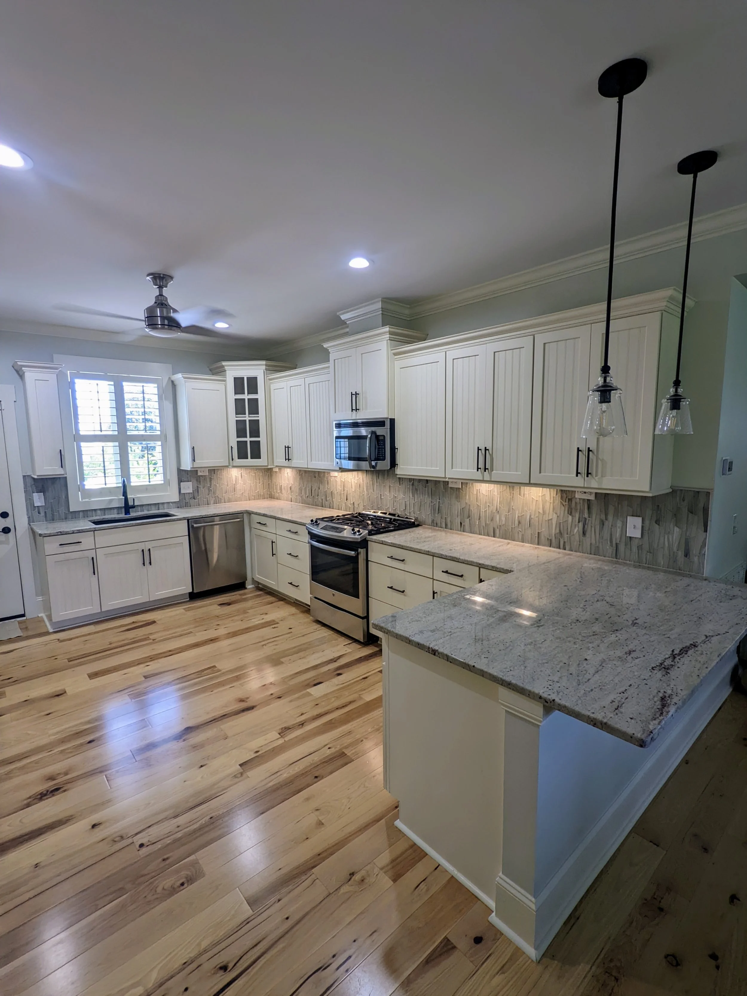 Kitchen with white cabinets, granite countertops, hardwood floors, stainless steel appliances, and pendant lights.