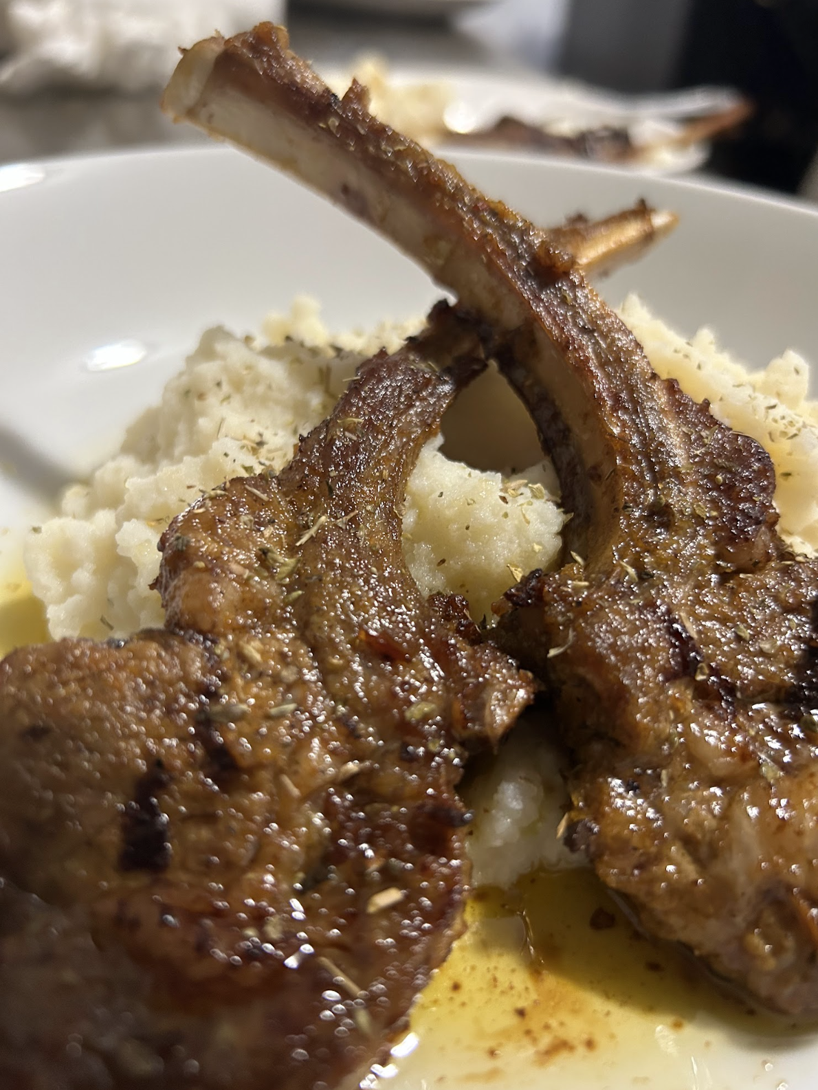 Grilled lamb chops served with mashed potatoes and garnished with herbs on a white plate; a dish by Nikee Catering.