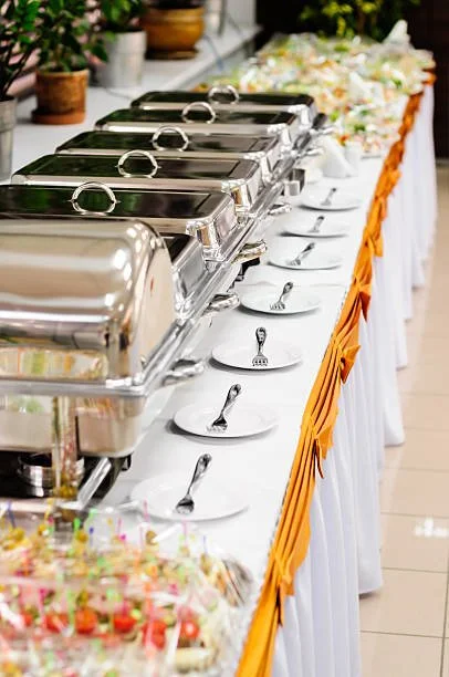 Buffet table with chafing dishes, white plates, and utensils at a catered event.
