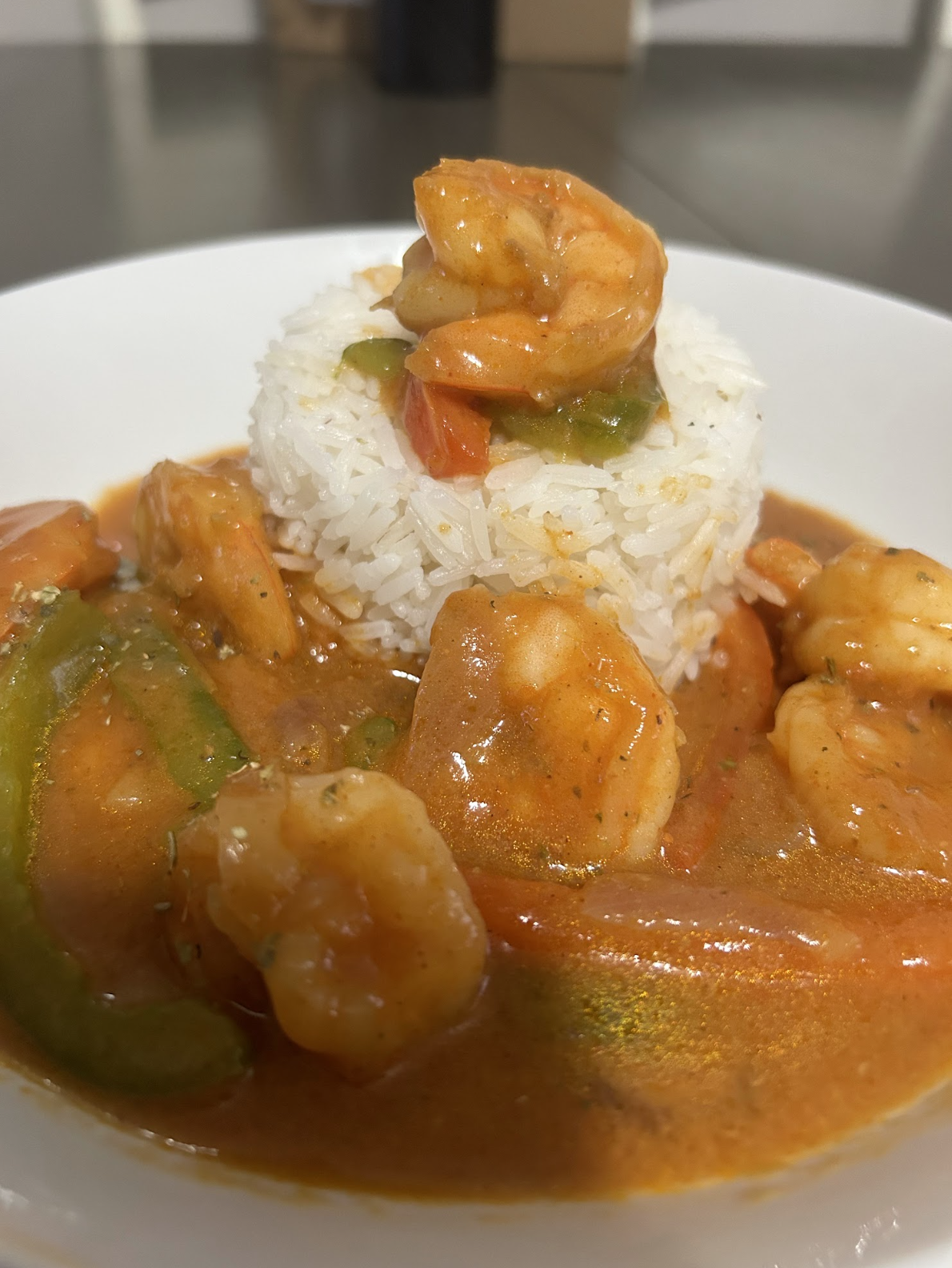 Close-up of a plate with rice and shrimp in orange sauce, garnished with green peppers and vegetables; a dish by Nikee Catering.