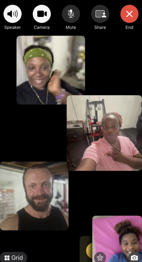 A screenshot of a video call with five participants: a woman with a green headband smiling, a woman in a pink shirt with a hand on her chest, a man with a beard and a black tank top, a young woman lying on a pink bed with a smile, and a woman with glasses and a dark top, all in different indoor settings.