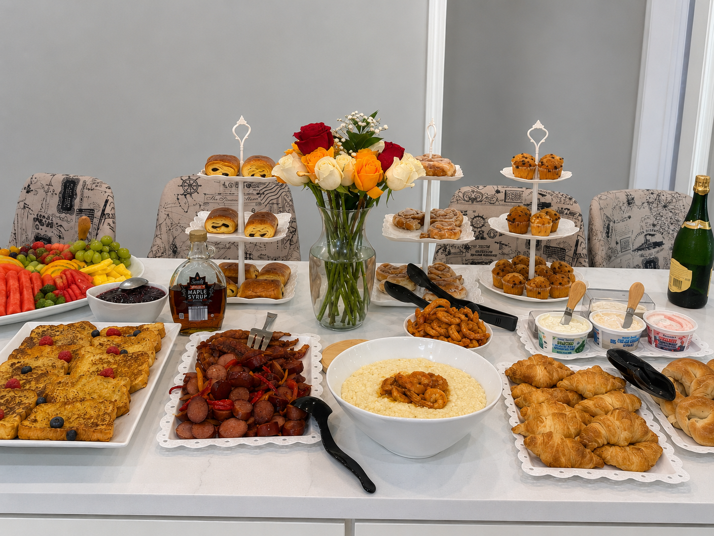 A table, catered by Nikee Catering, set for breakfast with various baked goods, fresh fruit, and condiments, centered around a vase of colorful roses.
