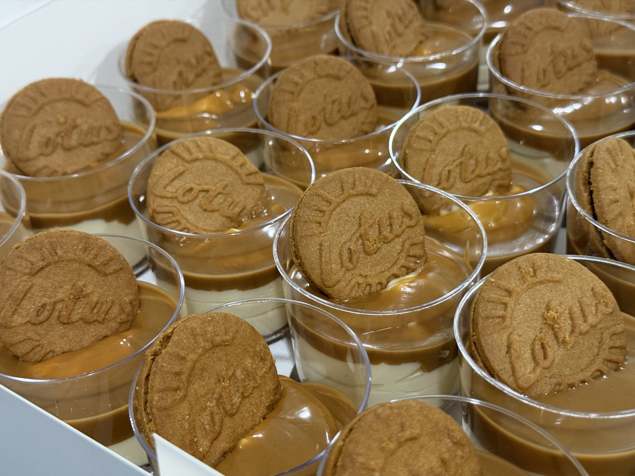 Multiple small clear plastic cups filled with caramel pudding topped with a digestive cookie, catered by Nikee Catering.
