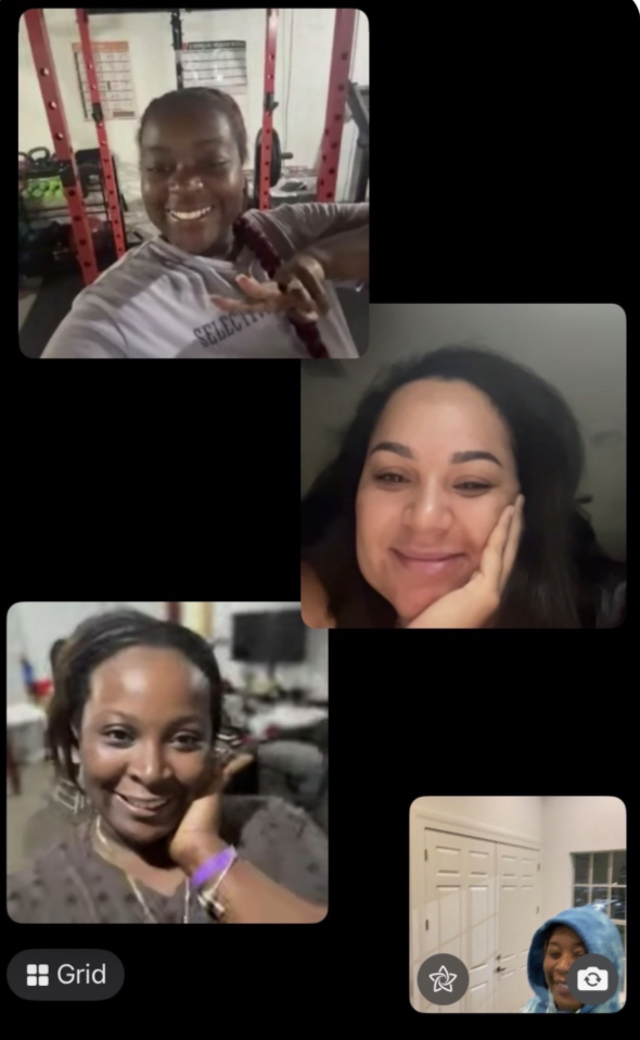 Four women engaged in a video call, each in different settings. The woman at the top left is in a gym, smiling and holding a strap over her shoulder. The woman at the top right has dark hair, is smiling, and resting her face on her hand. The woman at the bottom left has short hair, is smiling, and resting her face on her hand. The woman at the bottom right is in front of a white door, wearing a blue hoodie and smiling.