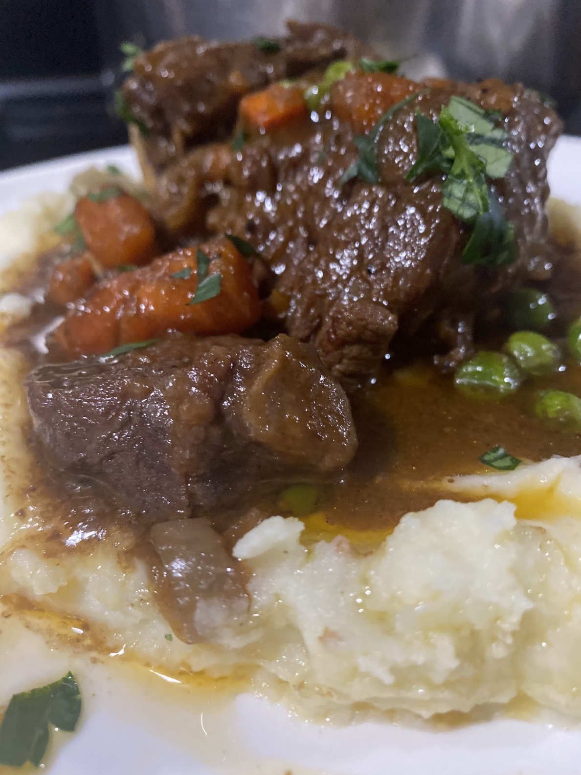 Hearty beef stew with carrots, peas, and herbs served over mashed potatoes; a dish by Nikee Catering.