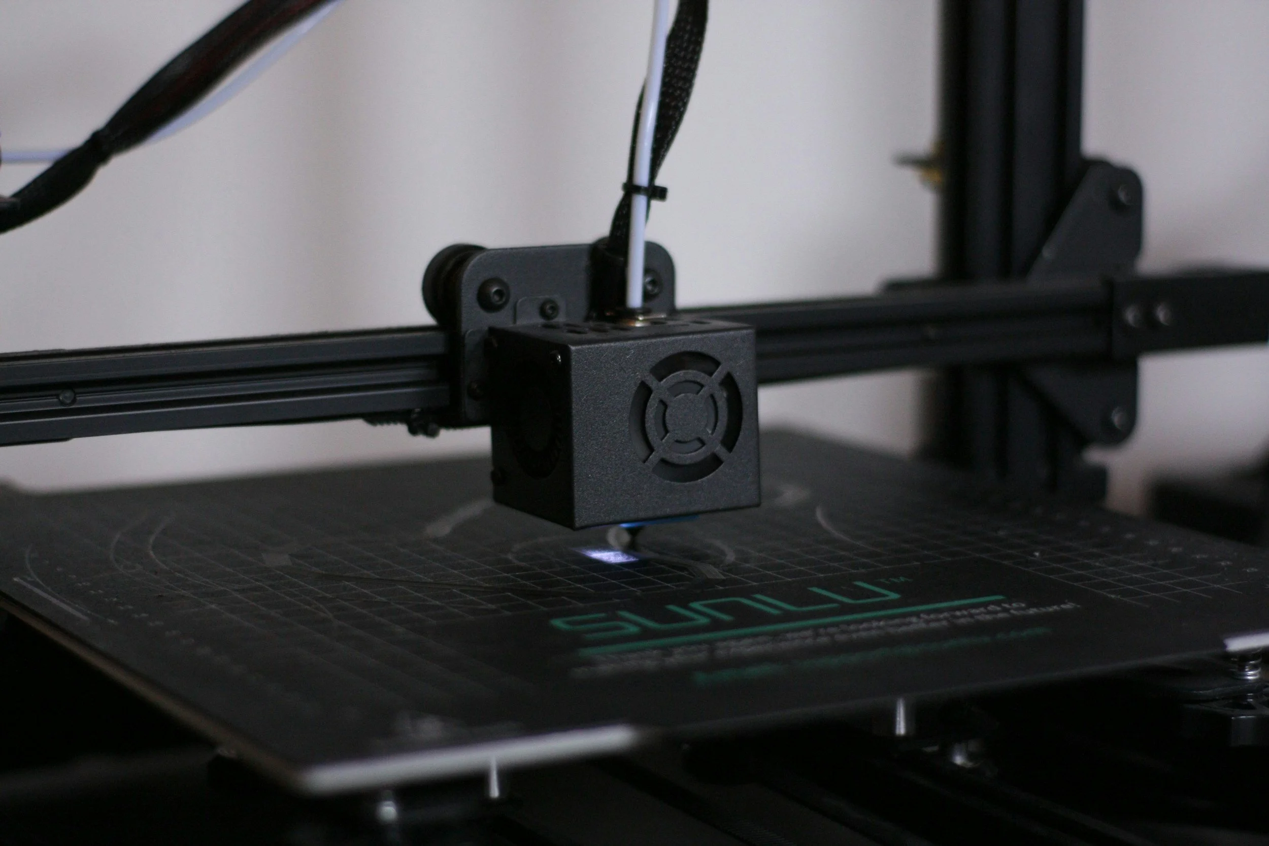 A 3D printer printing an object on a black print bed with a grid pattern.
