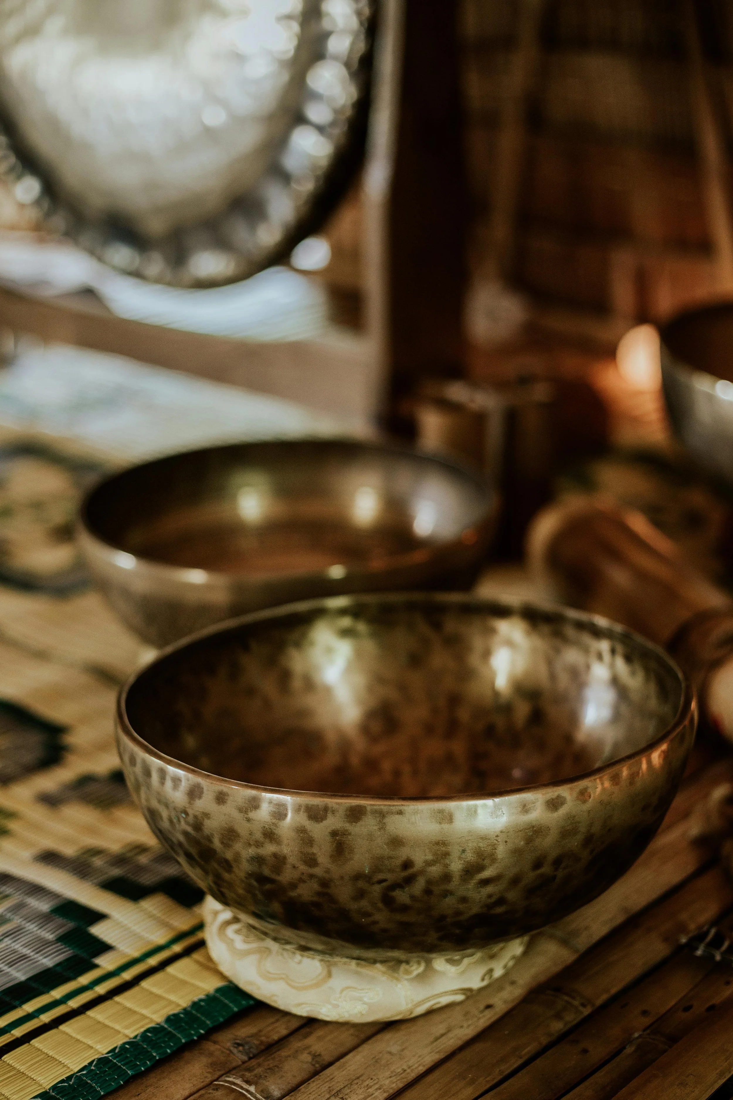 A close-up view of metallic Tibetan bowls placed on a woven mat, with a gong in the background, for a plant medicine ceremony.