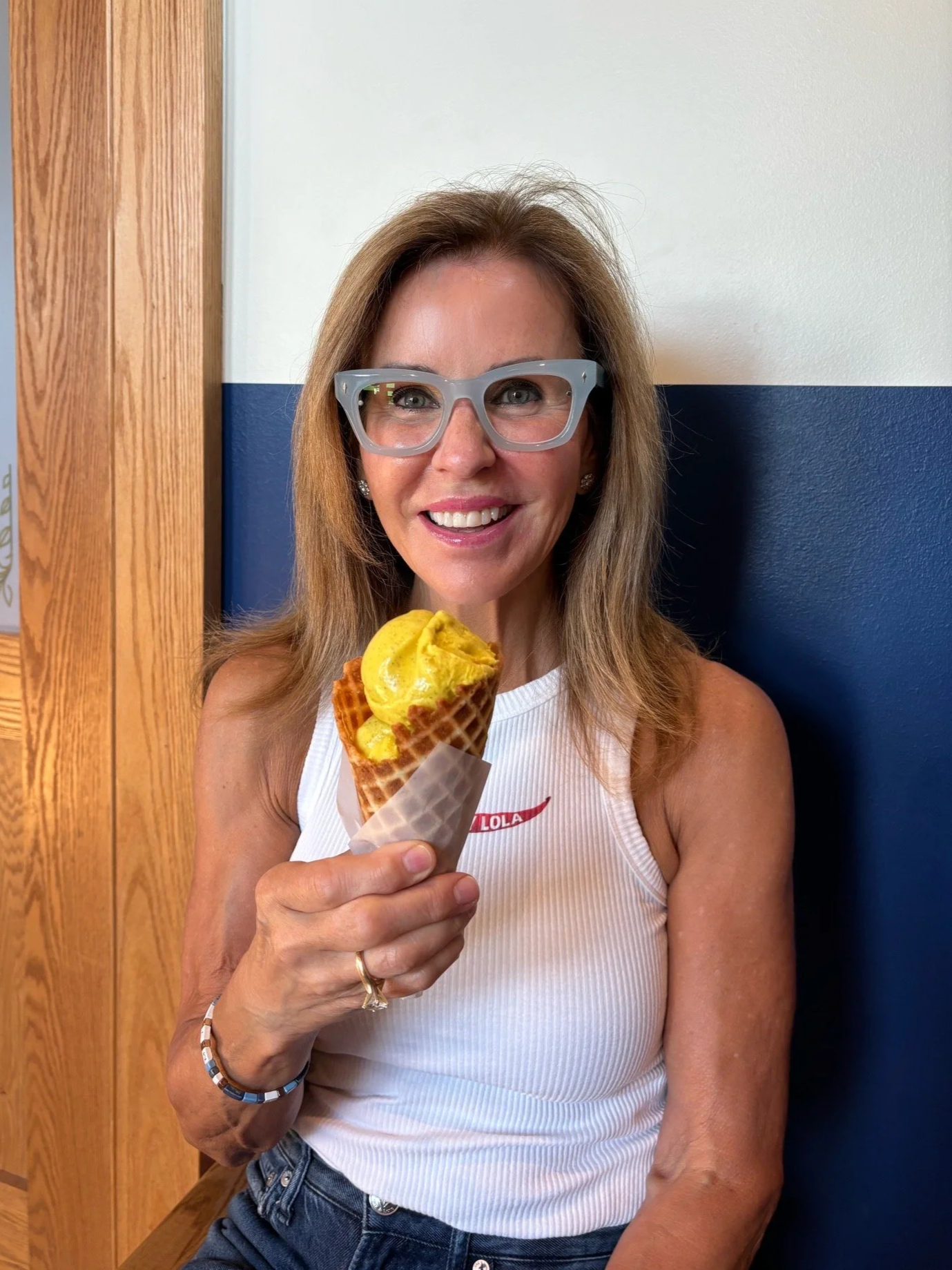 Pamela Kohll wearing glasses and a white sleeveless top holding a yellow ice cream cone with a waffle pattern and smiling at the camera.