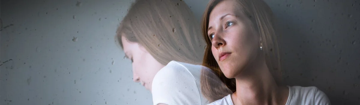 A woman with brown hair and earrings looking out of the window, with her reflection visible on the glass.