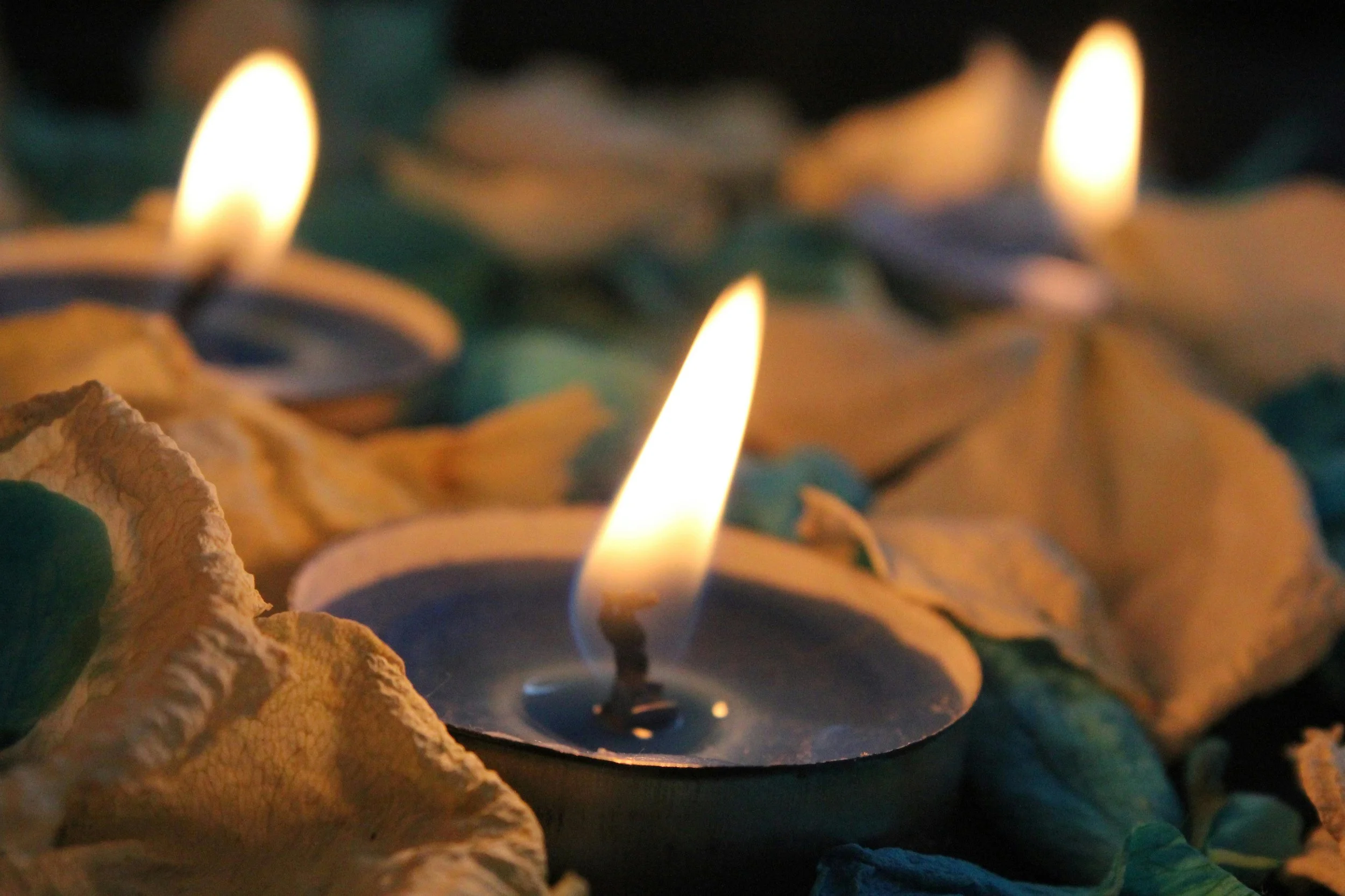 Three lit candles surrounded by dried leaves, creating a warm, peaceful atmosphere.