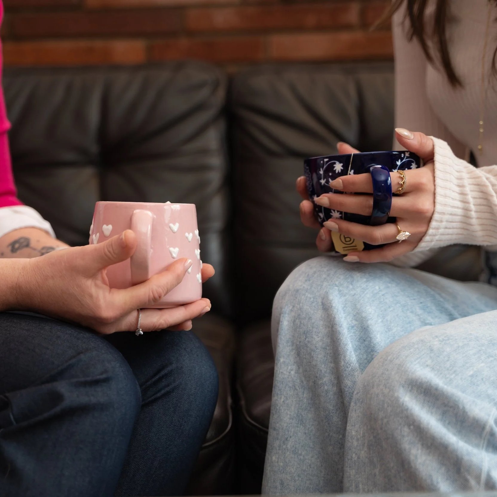 Two people holding hands on a white table, with one person holding a gray cup filled with coffee.