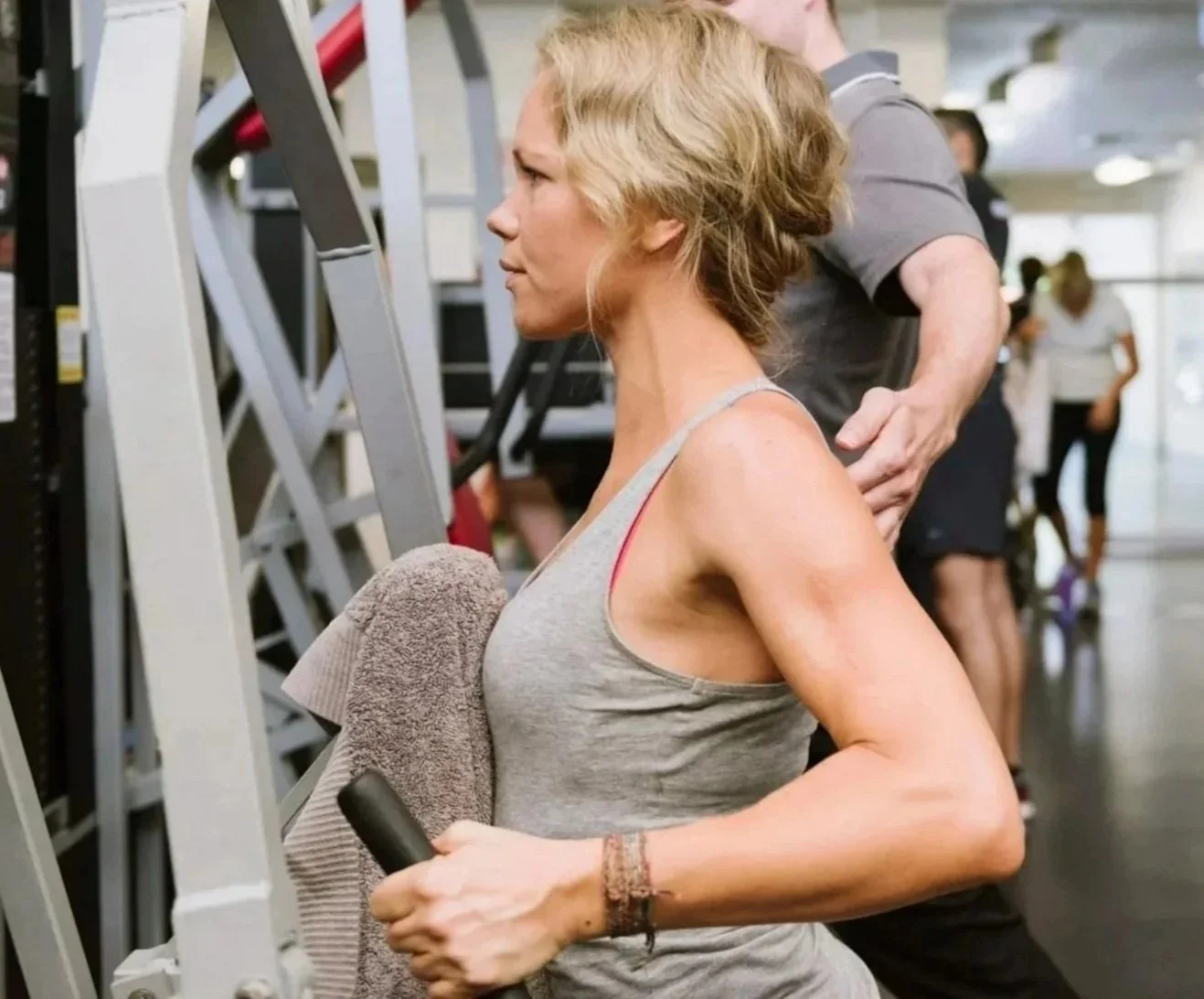 A woman exercising on a Pilates reformer machine in a bright, spacious room with large windows showing outdoor greenery.