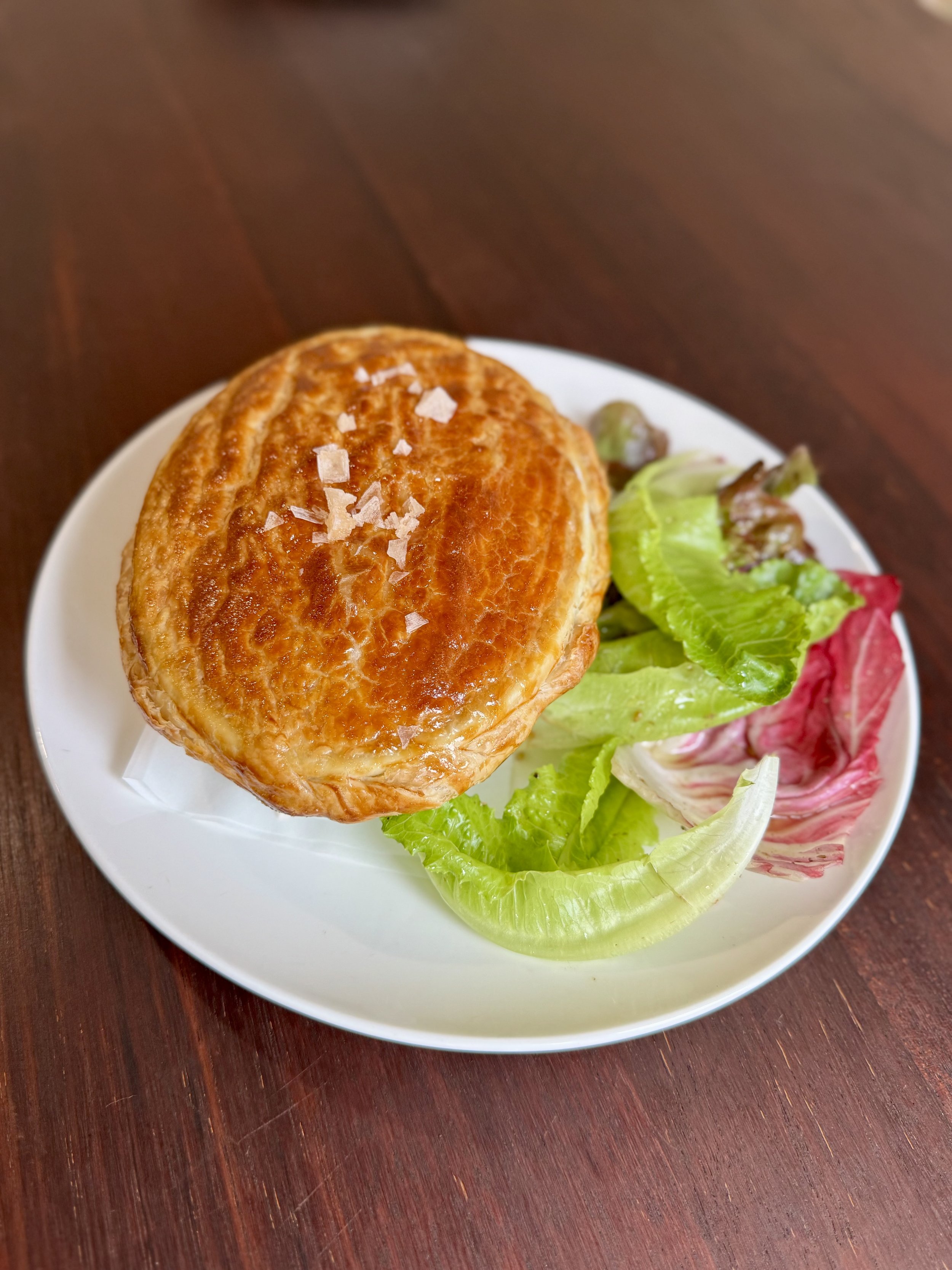 Baked puff pastry with coarse salt on top, served with mixed greens on white plate.