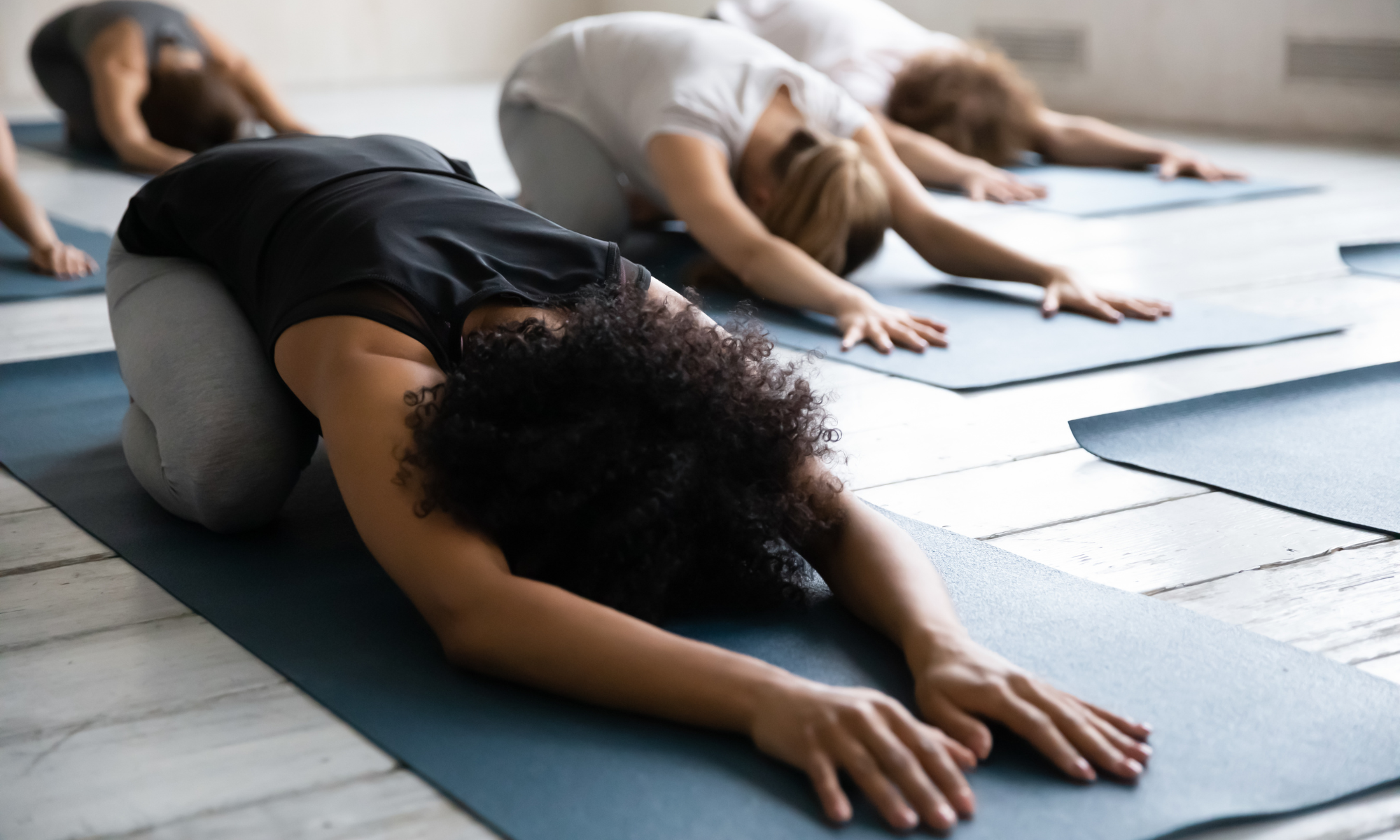 Group of women practicing yoga in child's pose on mats in a bright studio.