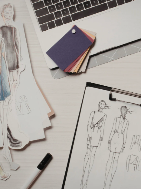 Fashion sketches and fabric swatches on a desk, with a laptop partially visible.