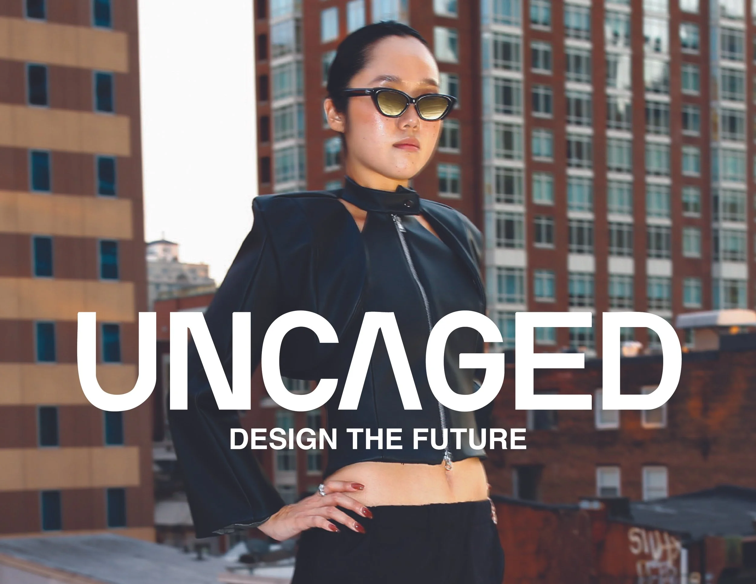 A woman with dark hair wearing sunglasses, a black cropped jacket, and high-waisted pants stands with her hand on her hip in front of city buildings. Text overlay says "UNCAGED" and "DESIGN THE FUTURE".