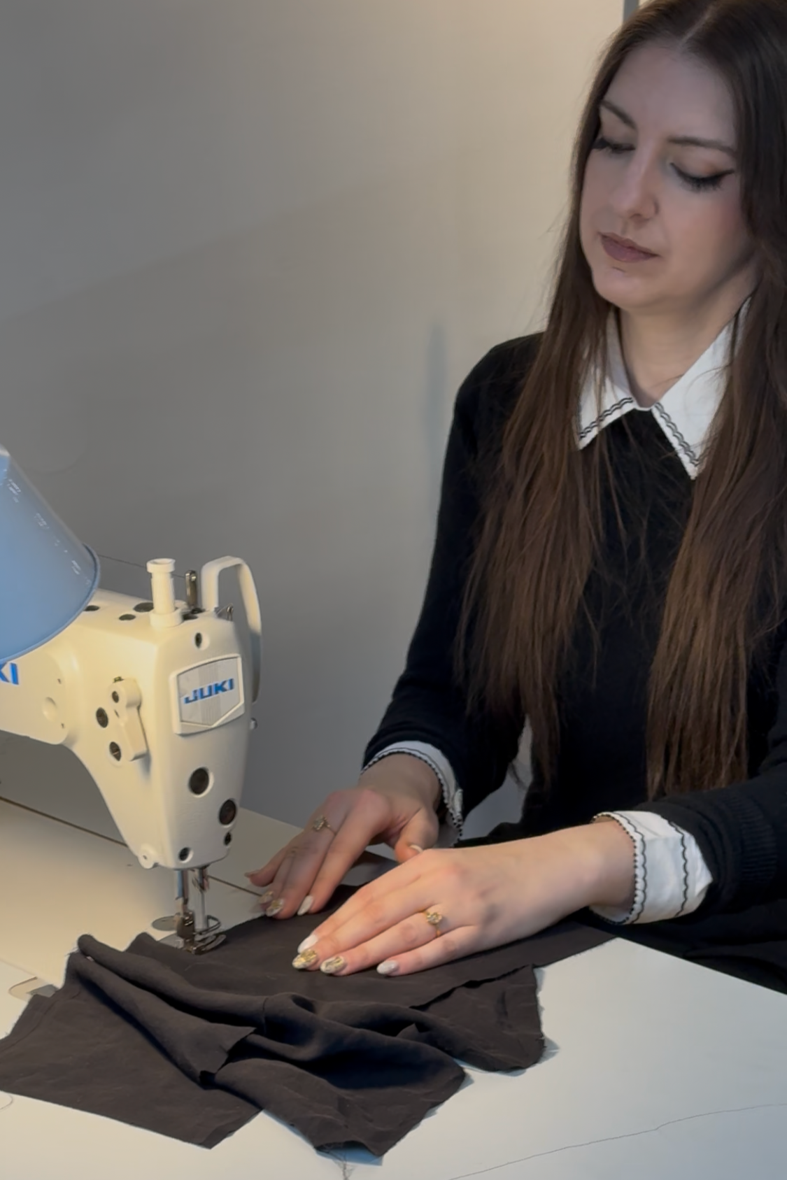 A woman sewing on a Juki industrial sewing machine, working on a black piece of fabric.