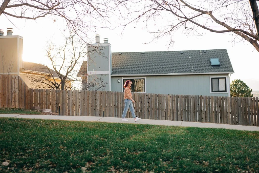 Becca Meyers walking on a paved path outside, with houses and a brown fence in the background and grass in the foreground