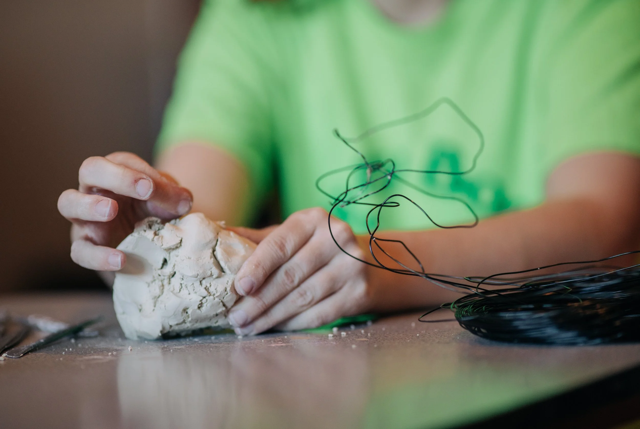Person using their hands to work with clay and black wire on a grey table surface