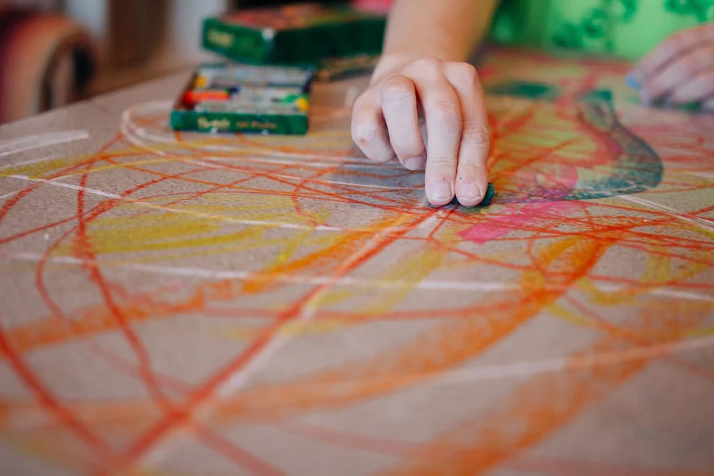 Person's hand using oil pastels and drawing on a grey tabletop