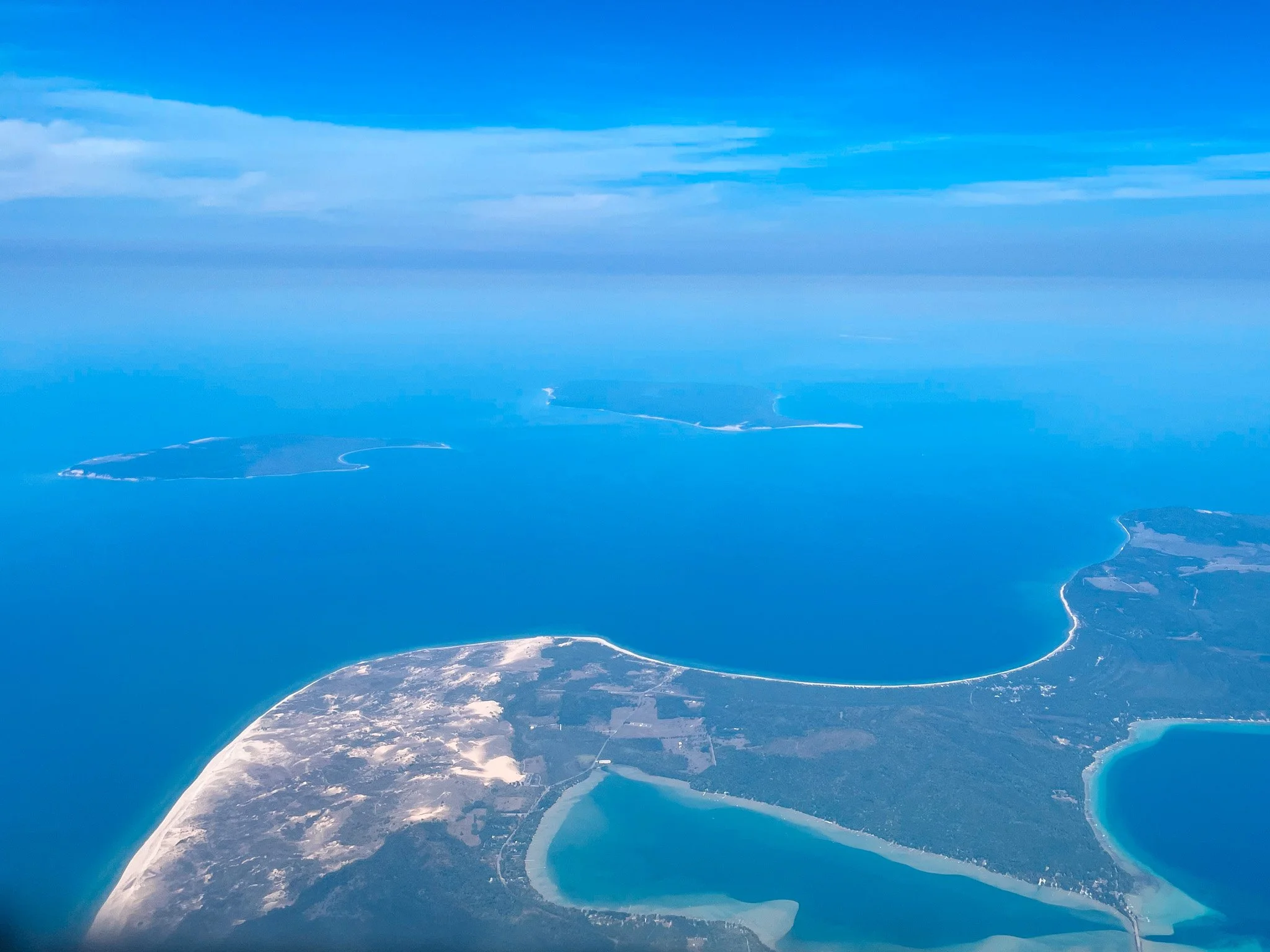 Aerial view of a coastline with bays, peninsulas, and islands surrounded by blue ocean under partly cloudy sky.