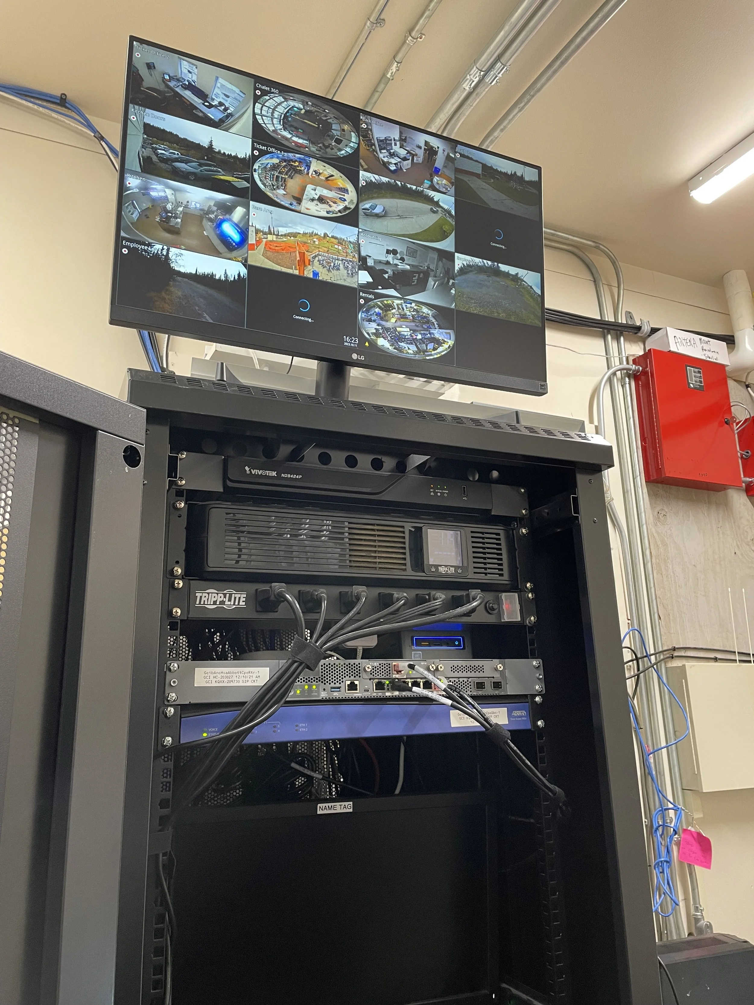 Surveillance monitor displaying multiple security camera feeds above a server rack in a control room.