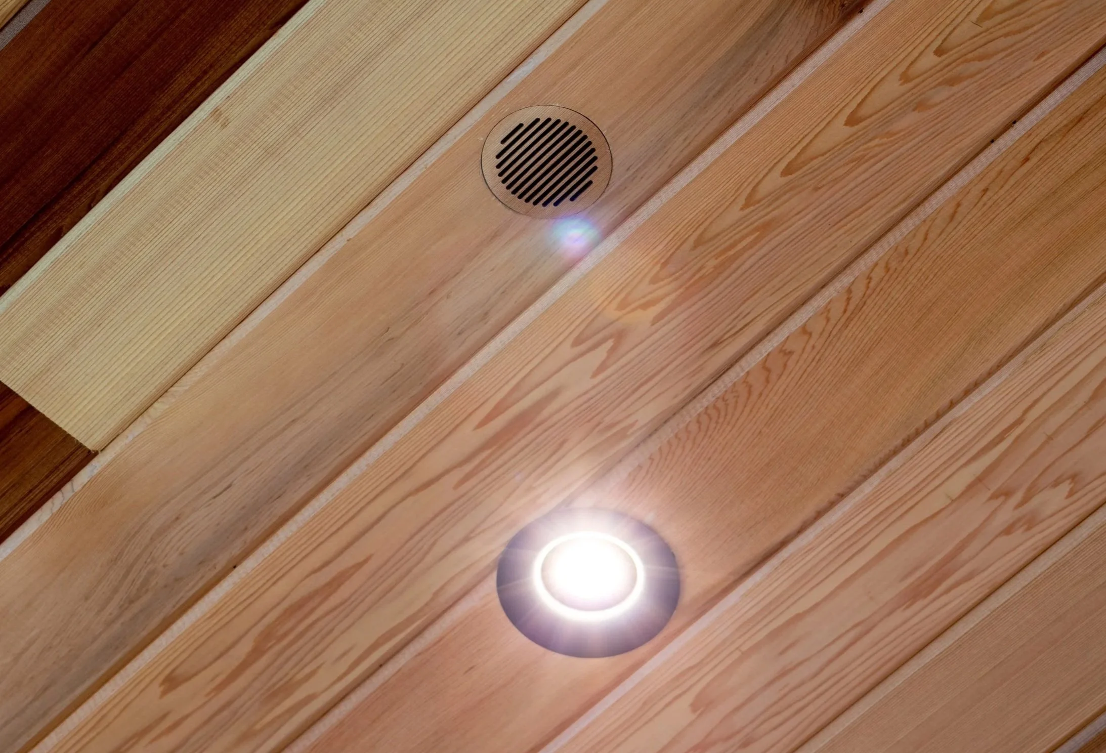 Ceiling with wooden planks, a centered round air vent grille, and a recessed ceiling light