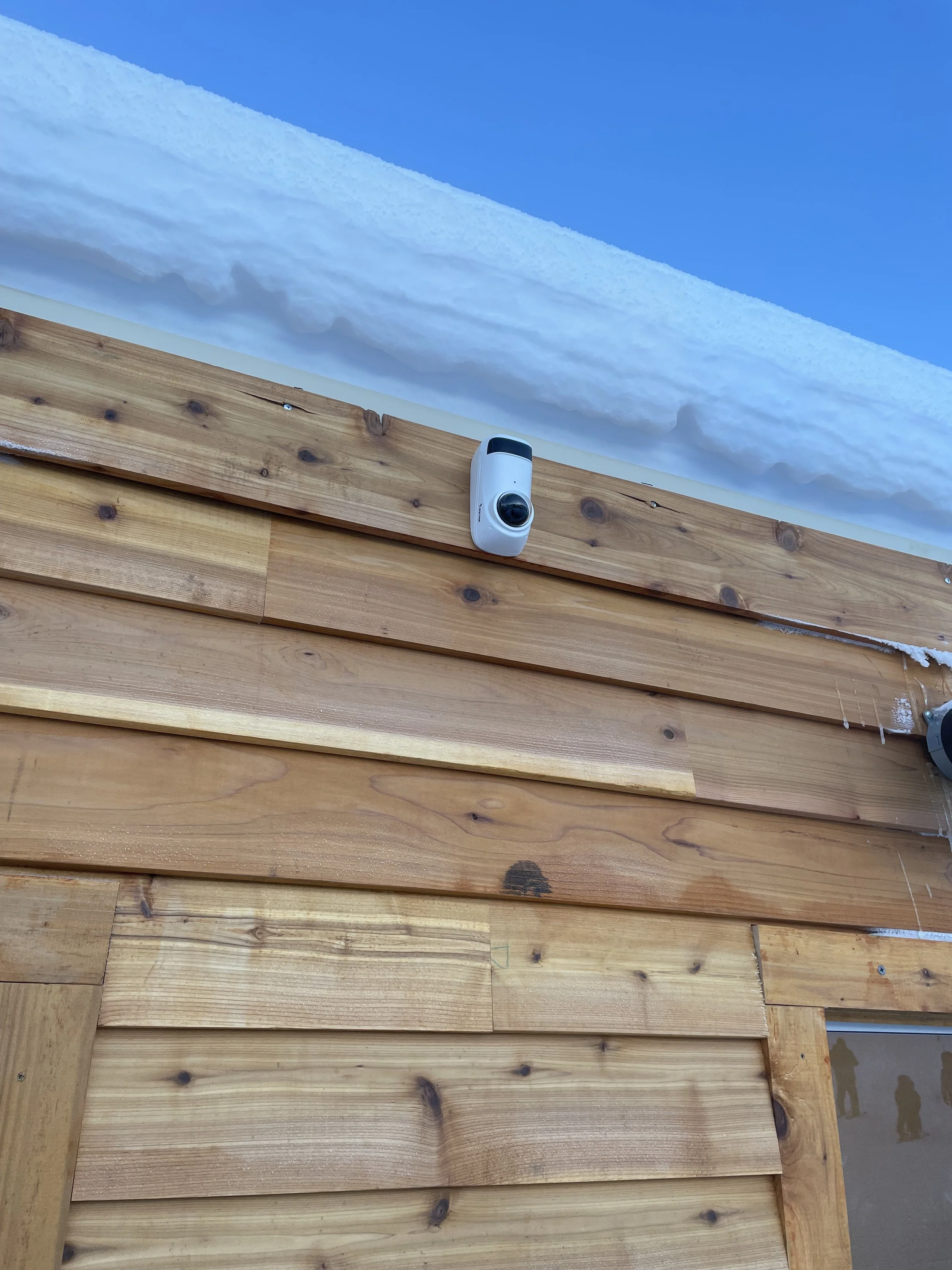 A snow-covered roof with two security cameras mounted on a wooden exterior wall.