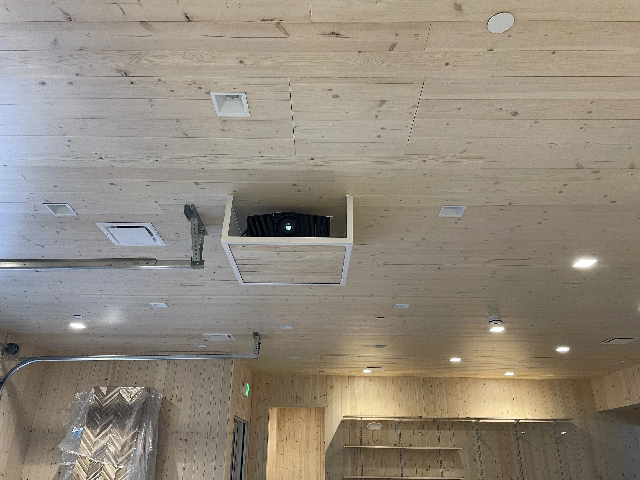 In 49th State Brewing's Tasting Room, a custom projector mount featuring the same wood as the tongue and groove ceiling hosts a Sony 4K HDR Laser Projector. The ceiling features evenly-distributed recessed lights.