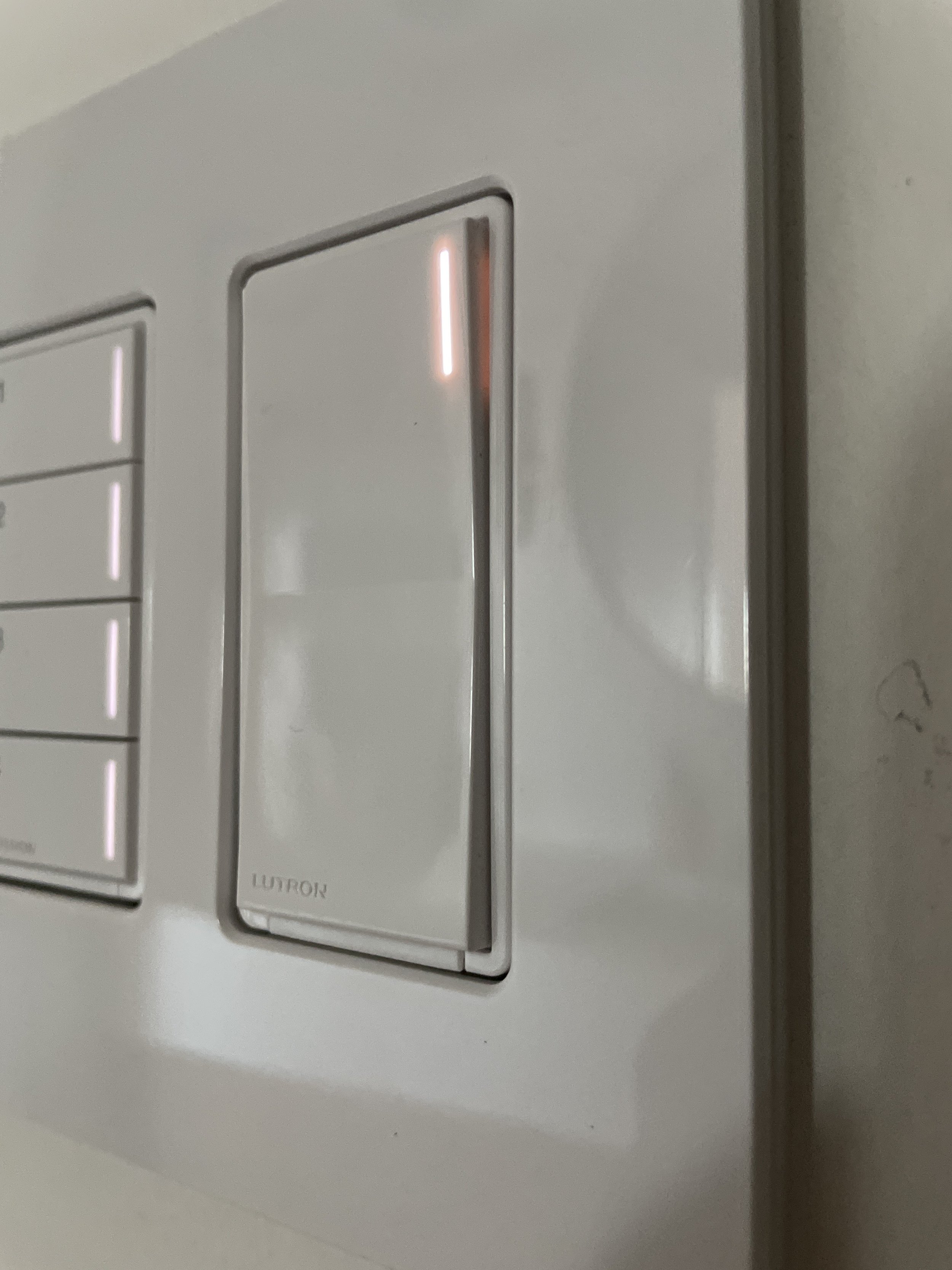 Close-up of a white Lutron light switch with an illuminated red indicator light.