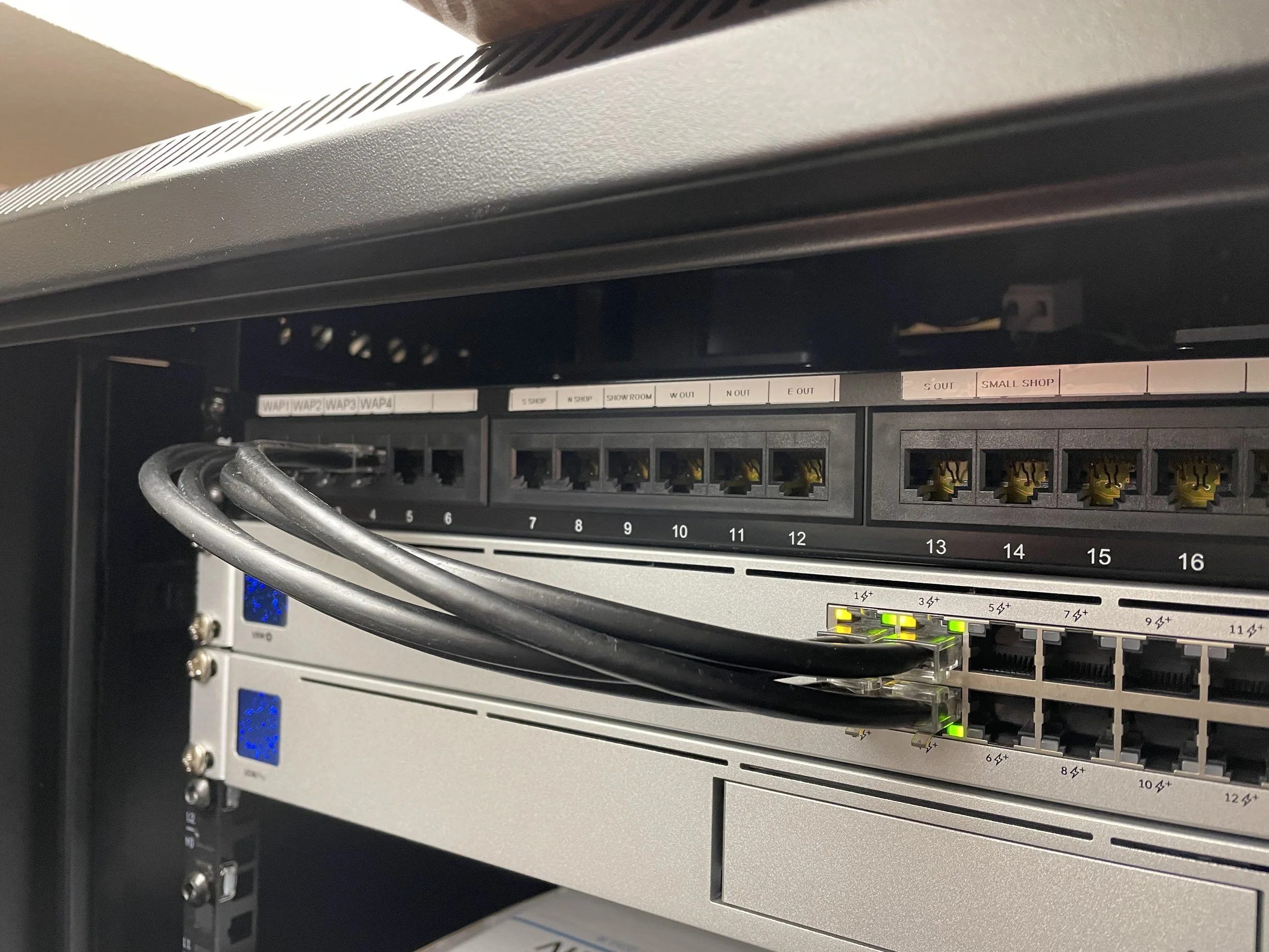Close-up of a network server rack with Ethernet cables plugged into ports, green LED indicators, and labels above the ports.