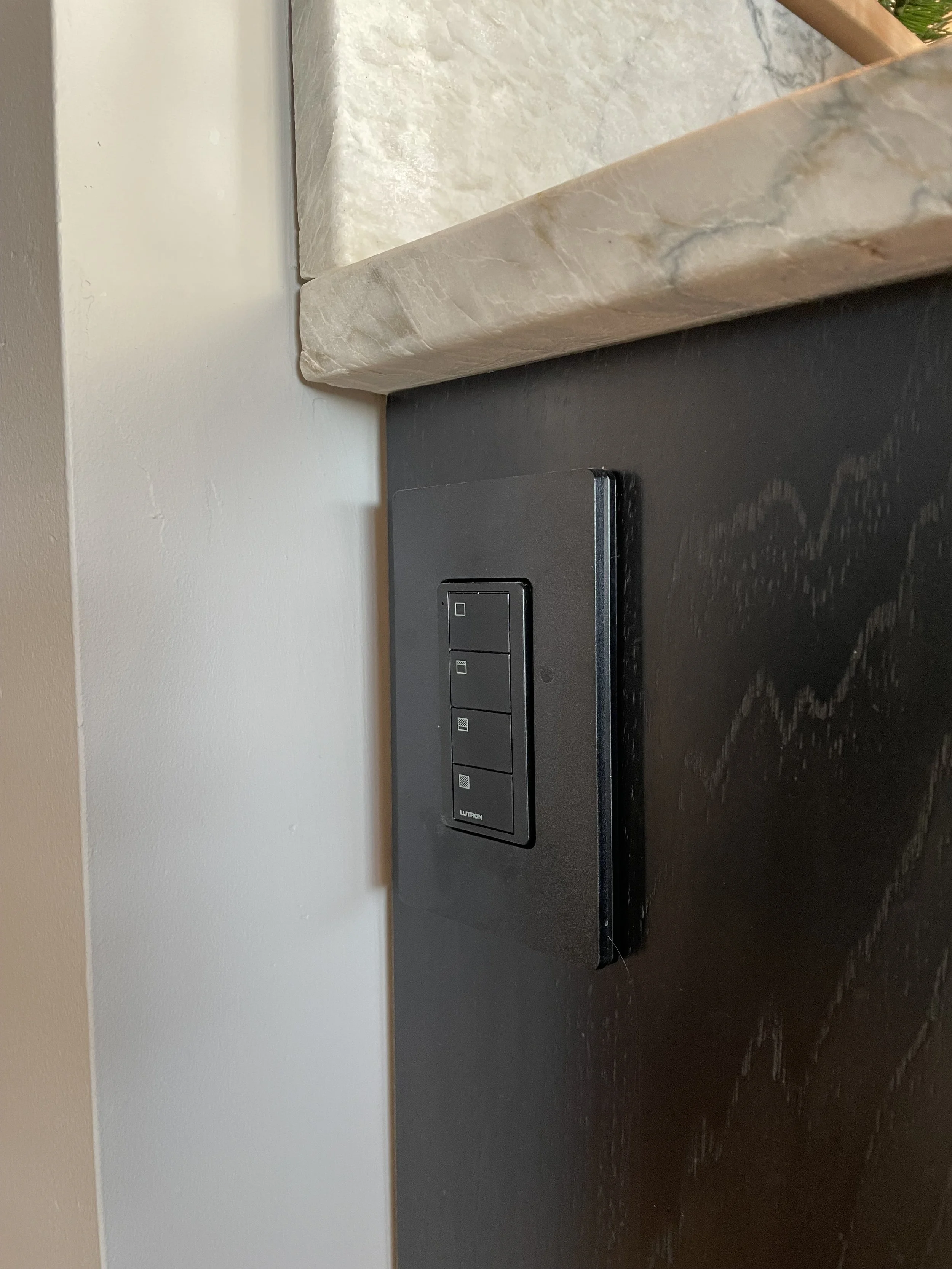 Black control panel with four rectangular switches mounted on a dark wall next to a beige marble countertop.