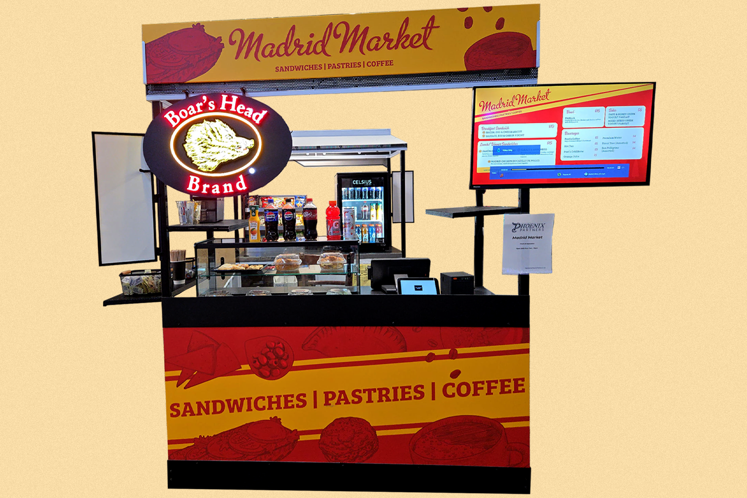 A food stand named Madrid Market offering sandwiches, pastries, and coffee. The stand features a Boar's Head brand sign, a display of bottled sodas and condiments, and a digital menu board. The background has a yellow sign with red and purple lettering.