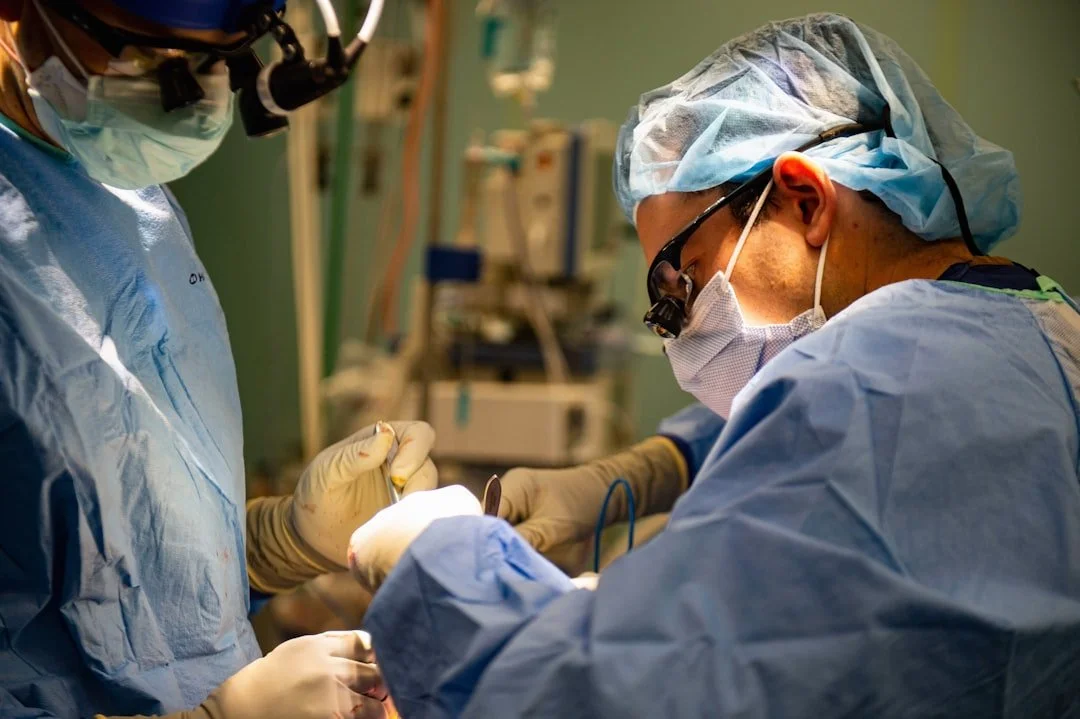 Two surgeons in surgical gowns, masks, and gloves perform surgery in an operating room, focusing on the patient.