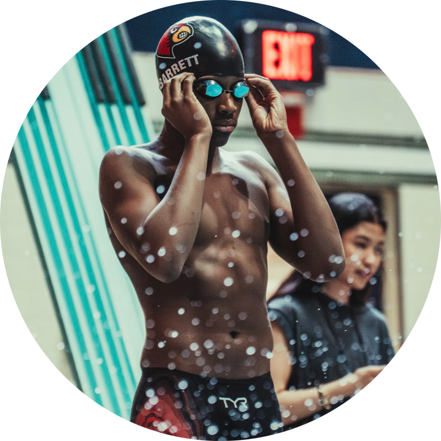 Noland is adjusting goggles before a race, wearing a swim cap and swim trunks