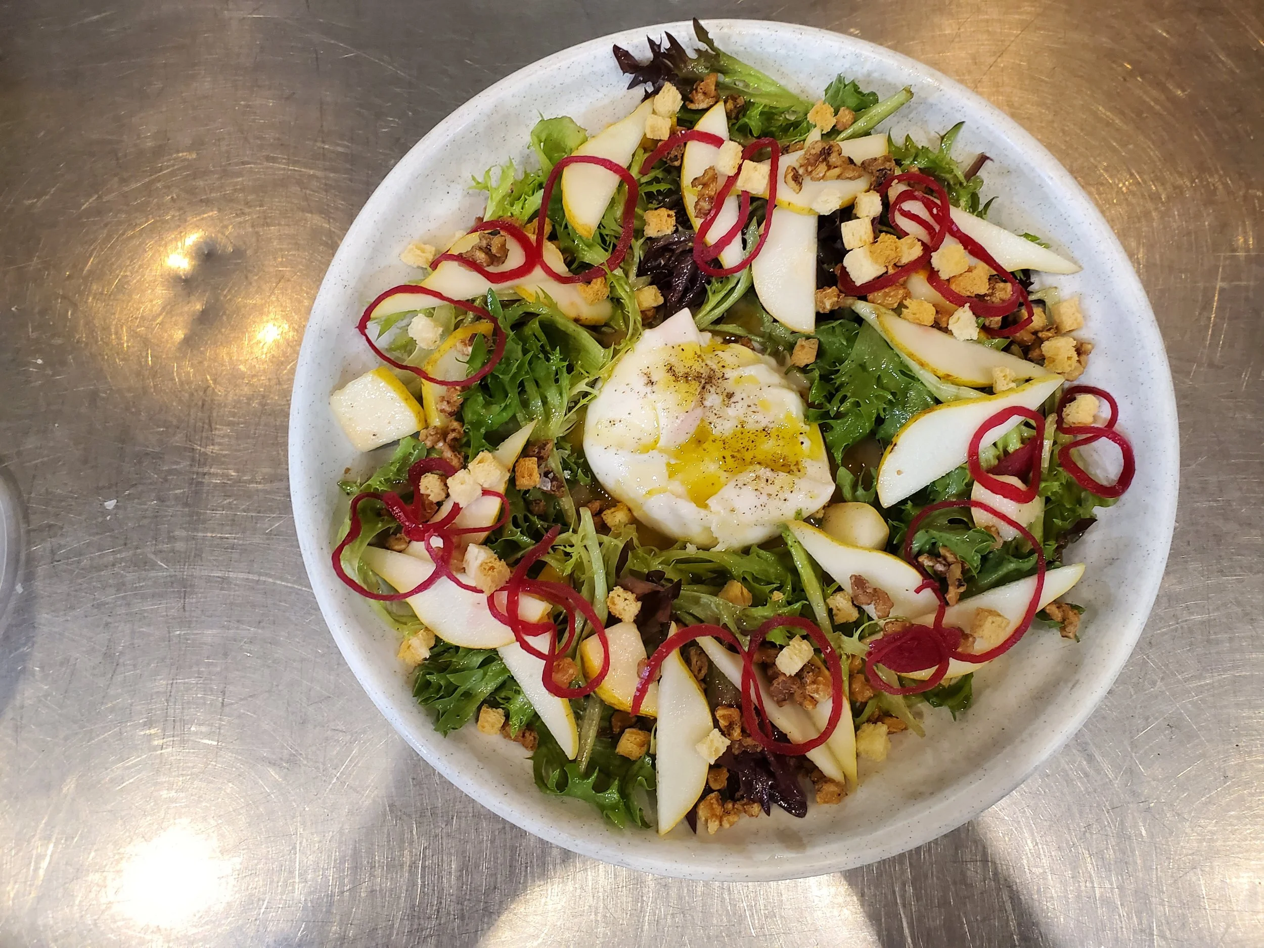 Salad with greens, sliced pears, red onion, crumbled nuts, and a piece of Burrata cheese, in a white bowl.