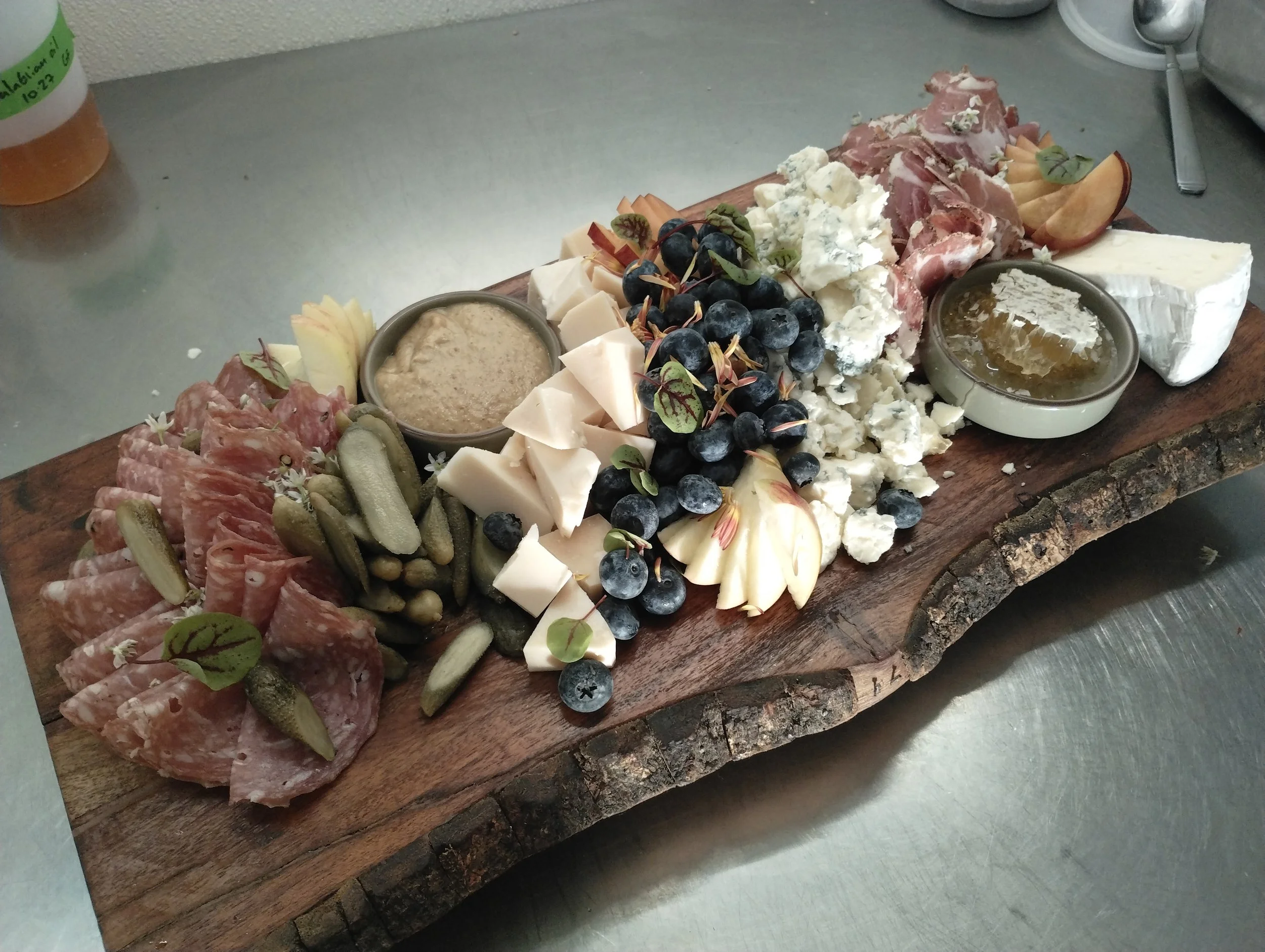 A wooden charcuterie board with assorted cheeses, cured meats, grapes, berries, and condiments.