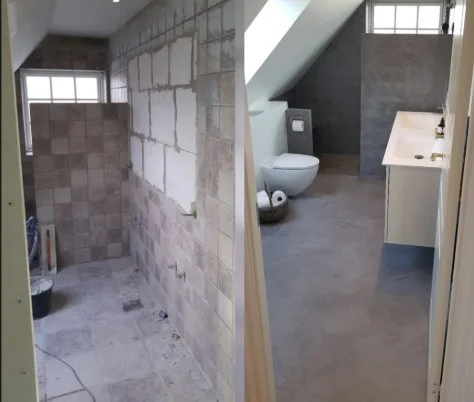 Comparison of a bathroom before and after renovation. The left side shows an unfinished space with exposed tile walls, construction tools, and debris. The right side displays a finished bathroom with gray flooring, modern toilet, sink, and a sloped ceiling.