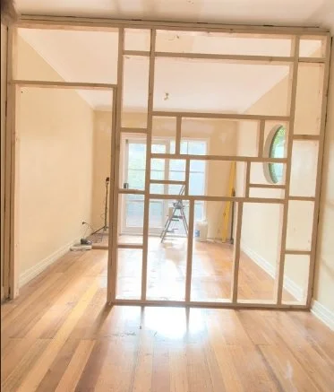 Interior room under construction with wooden framing for new wall and hardwood floors